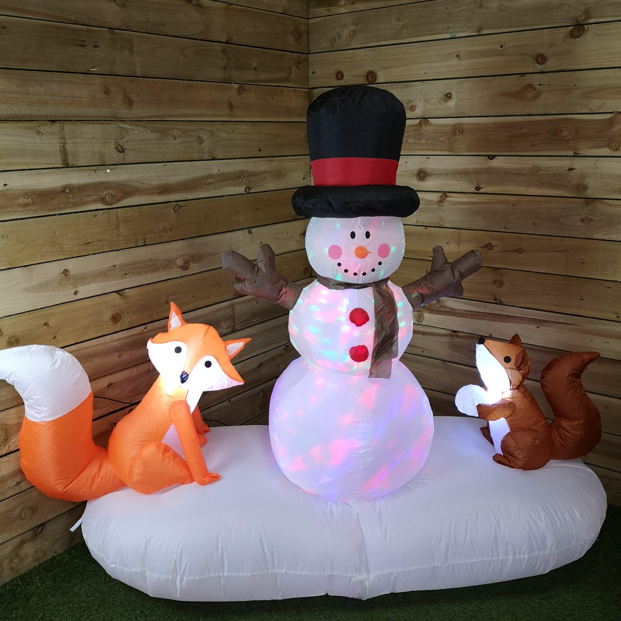 A 1.5m tall inflatable snowman with a black top hat and red scarf stands between a lit orange fox and a brown squirrel, all set on a white base in a wooden environment.