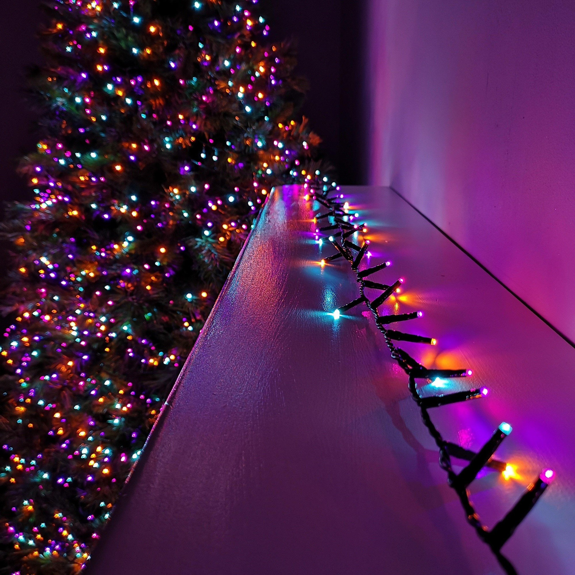 Colorful 12.5m LED string lights with a black wire, featuring vibrant rainbow hues, set against a softly lit backdrop of a decorated Christmas tree.