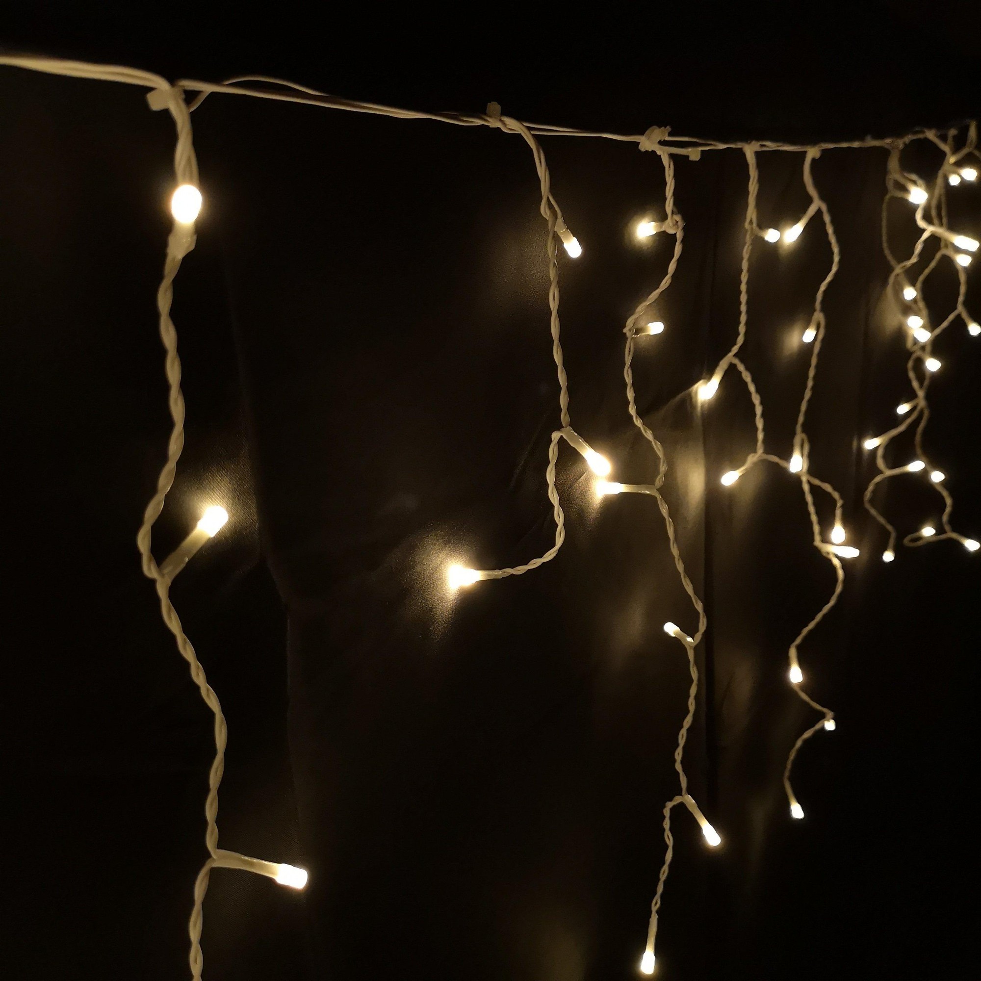 Warm white LED icicle lights on a white cord, featuring 16 meters of string with 8 different lighting functions, ideal for outdoor Christmas decoration.