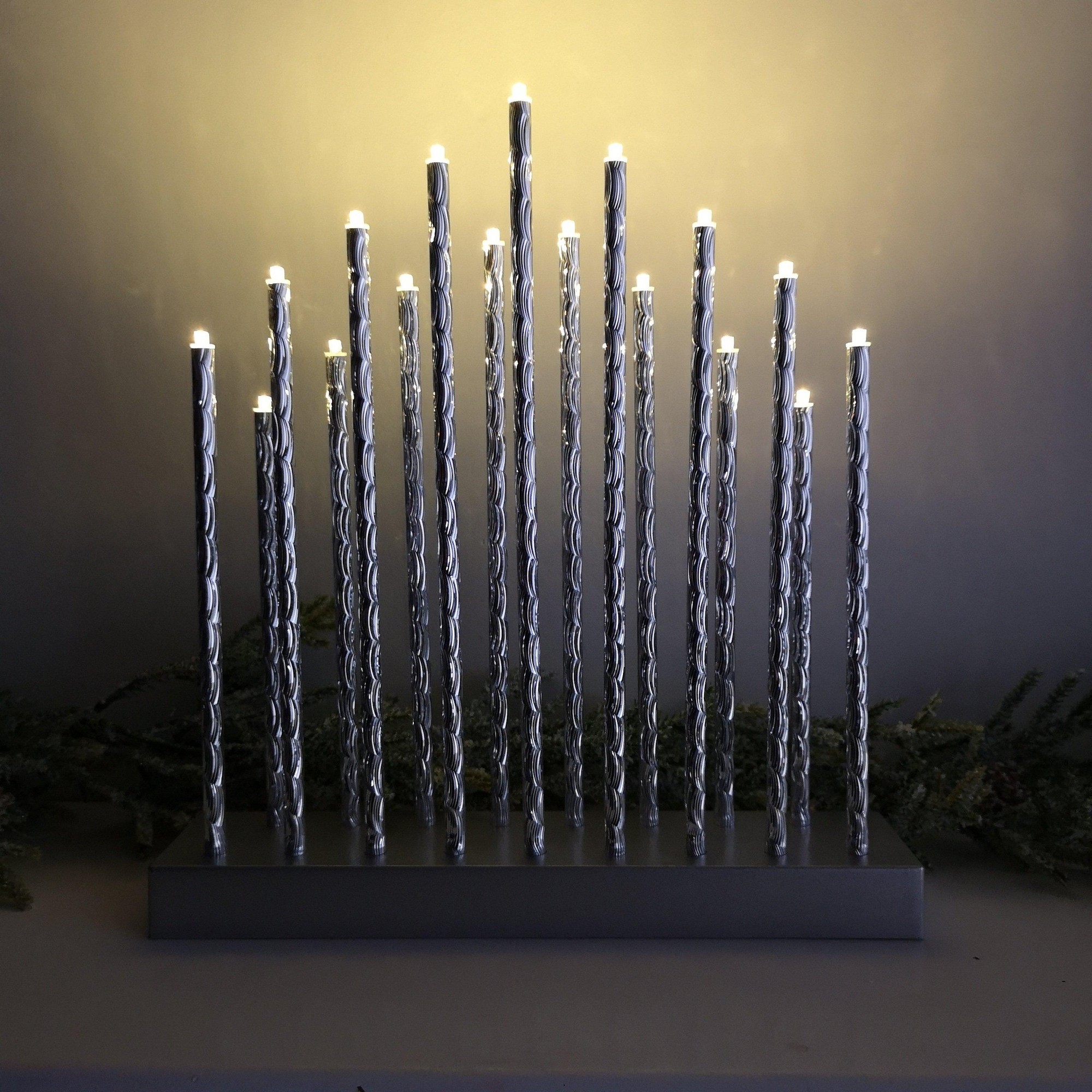 Premier's 29cm silver aluminium candlebridge features 17 LED lights on twisted candle-like stems, set on a sleek base, creating a festive ambiance.
