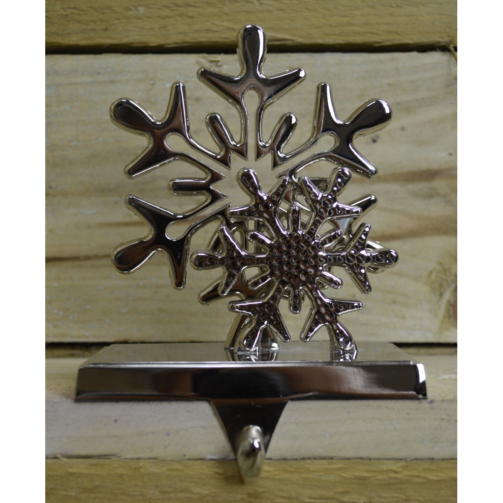 Silver snowflake design stocking hanger with intricate cutouts, featuring a sturdy base and a hook for hanging, set against a rustic wooden background.