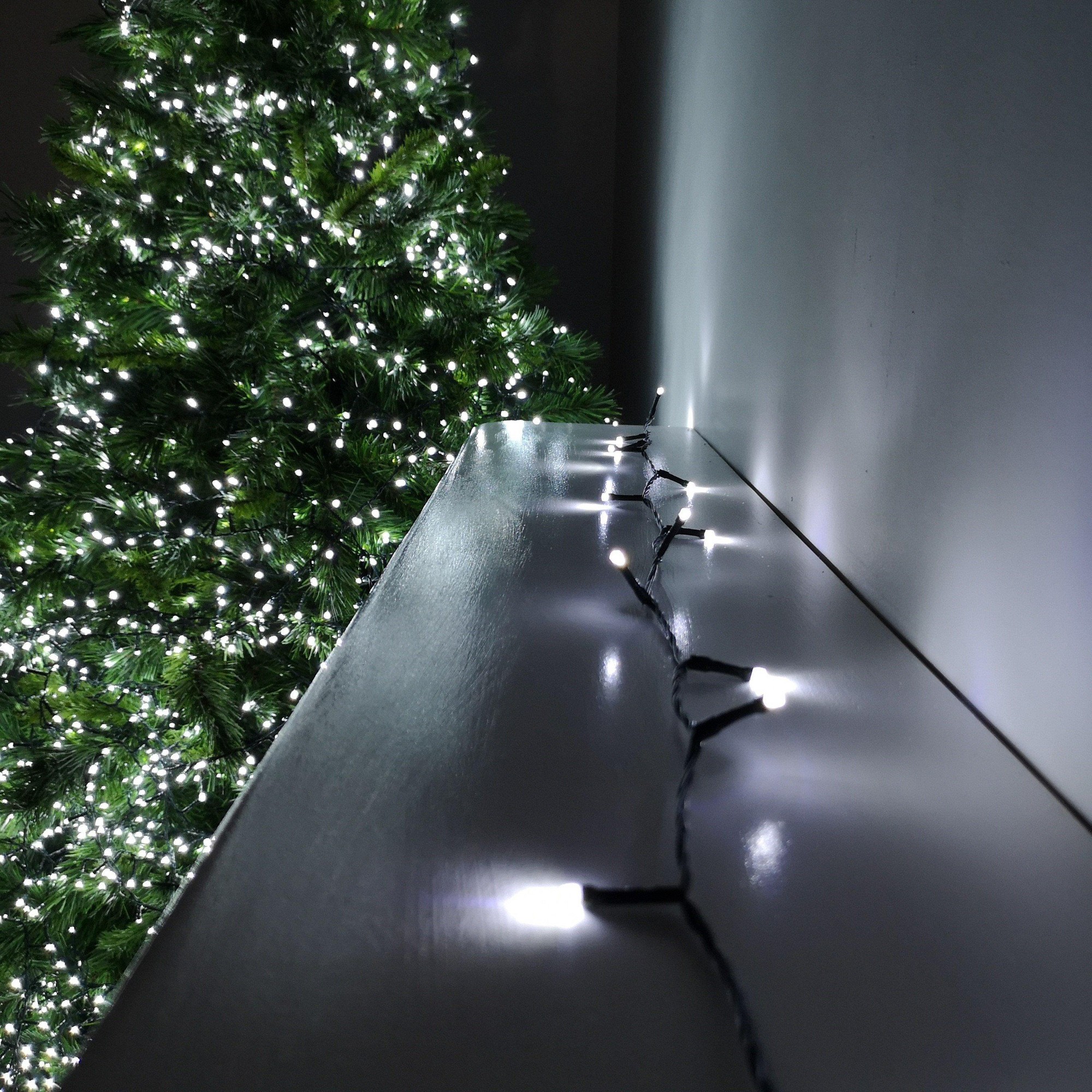 Cool white LED string lights on a black wire, featuring multiple functions and a timer, displayed alongside a lush green Christmas tree.