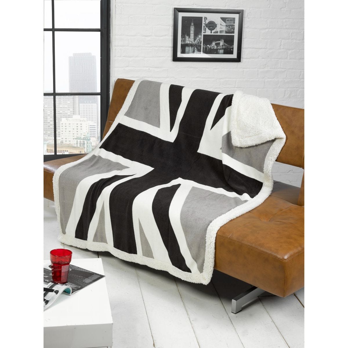 Black and grey Union Jack throw blanket with a soft, fluffy white backing, draped over a brown leather sofa, enhancing a modern living space.