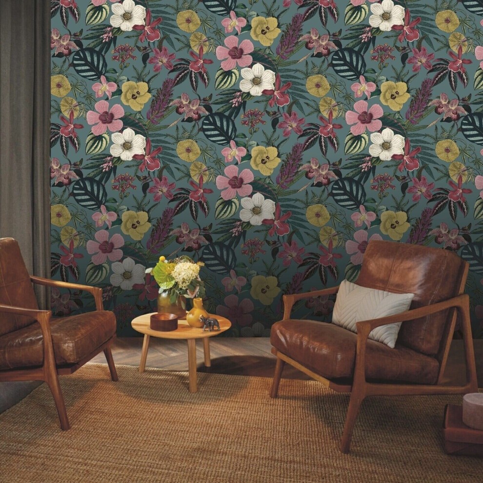 Rasch Priya Floral Petrol Wallpaper features a vibrant blue background adorned with colorful flowers and leaves, complemented by stylish brown leather chairs and a wooden table.