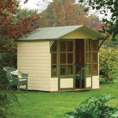 A brown timber summerhouse with green trim, featuring large front windows, a sloped roof, and a porch area, surrounded by lush greenery and outdoor seating.