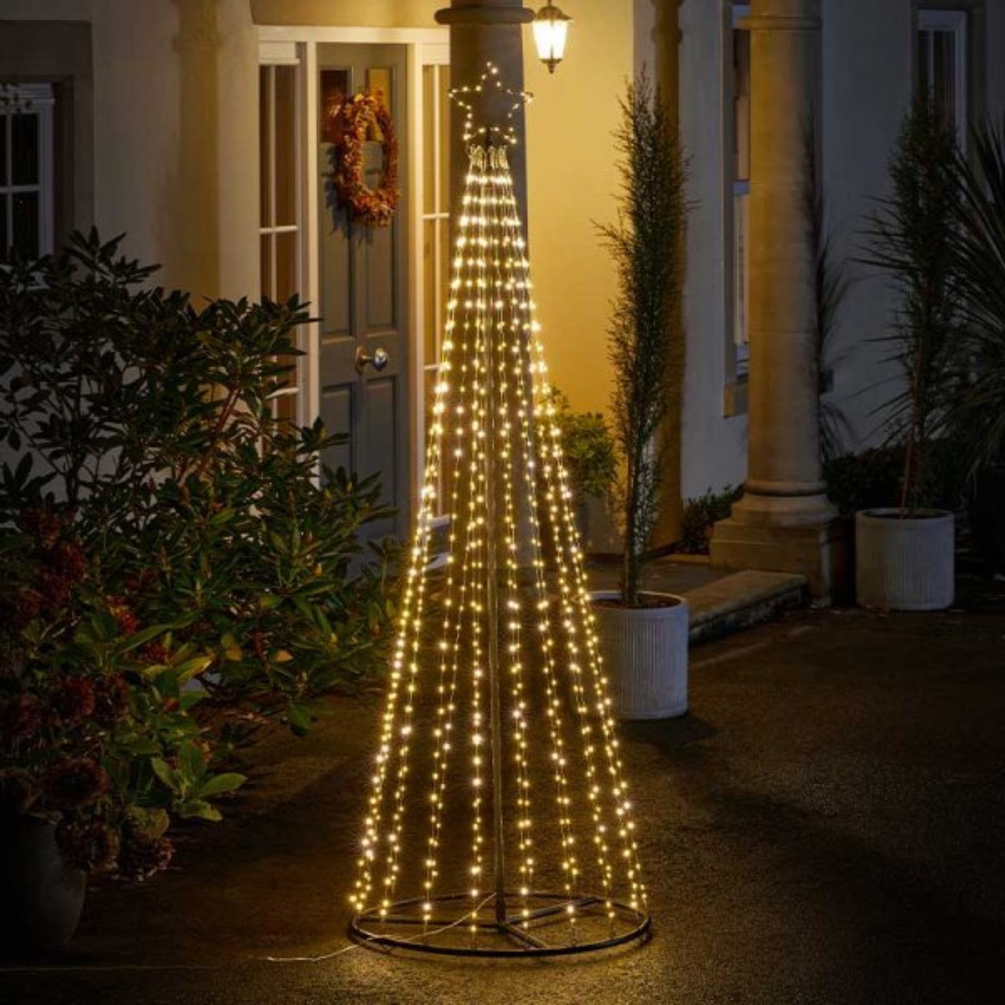 A 2.1m tall maypole tree with warm and cool white LED lights, featuring a star top, set against a porch with greenery and a wreath.