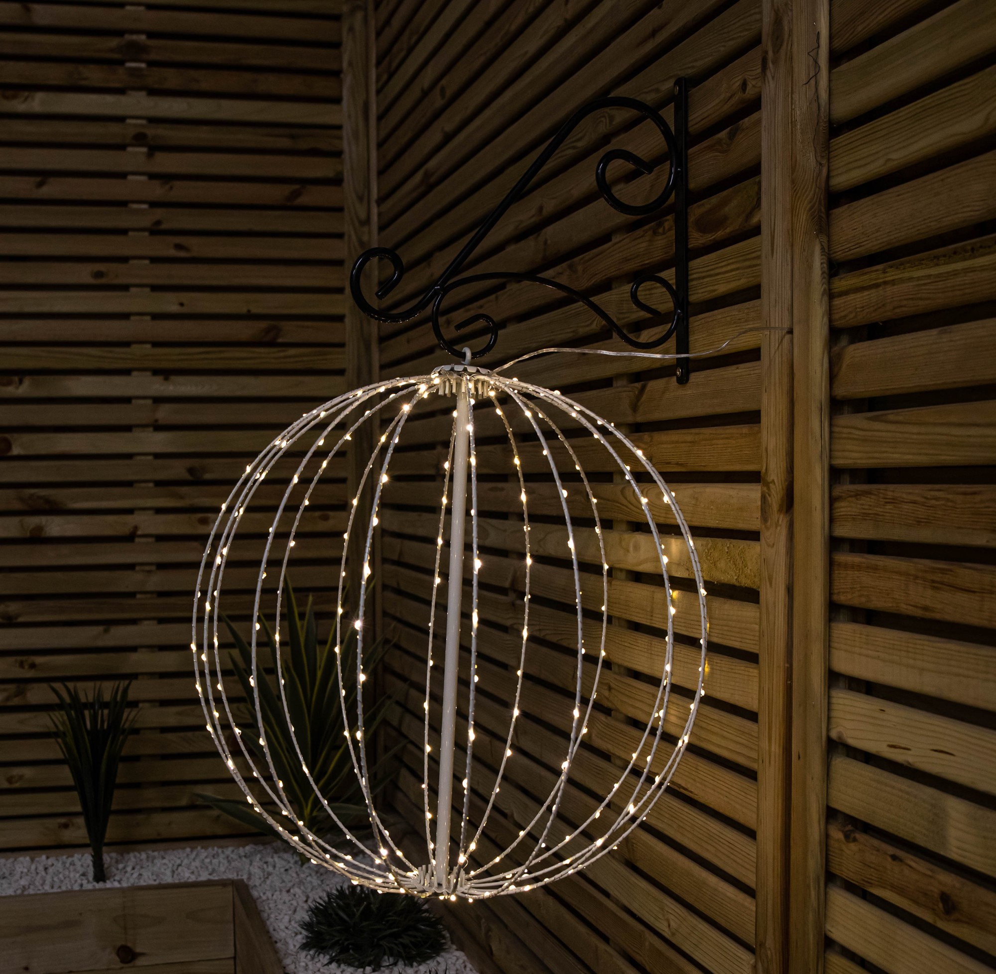 50cm white metal folding Christmas ball adorned with 256 warm white LEDs, elegantly hanging from a black decorative hook against a wooden backdrop.