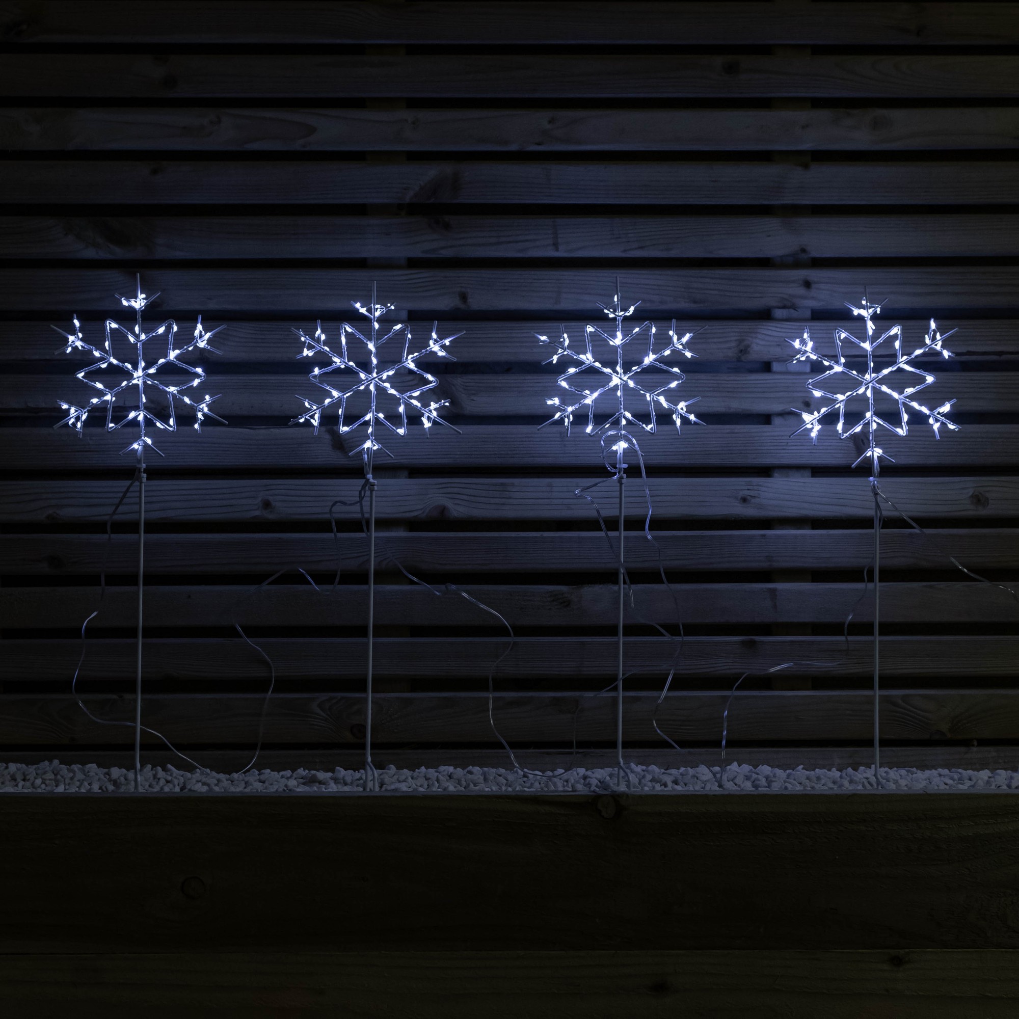Set of four 60cm white snowflake path lights featuring 260 bright white LEDs, mounted on slender stakes against a dark wooden backdrop.