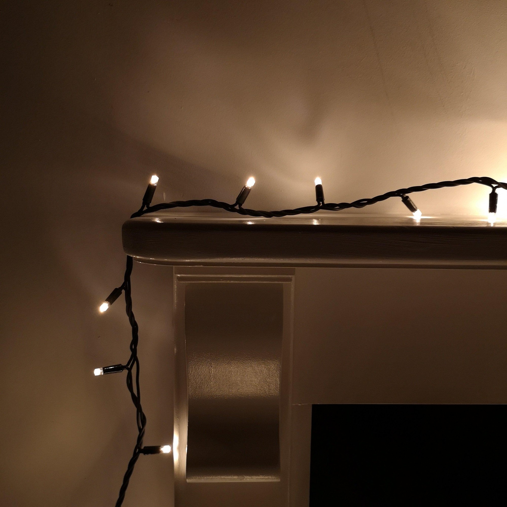 Warm white LED Christmas lights on a black cable, featuring 300 bulbs, connectable design, and a heavy-duty build, draped elegantly over a white mantel.