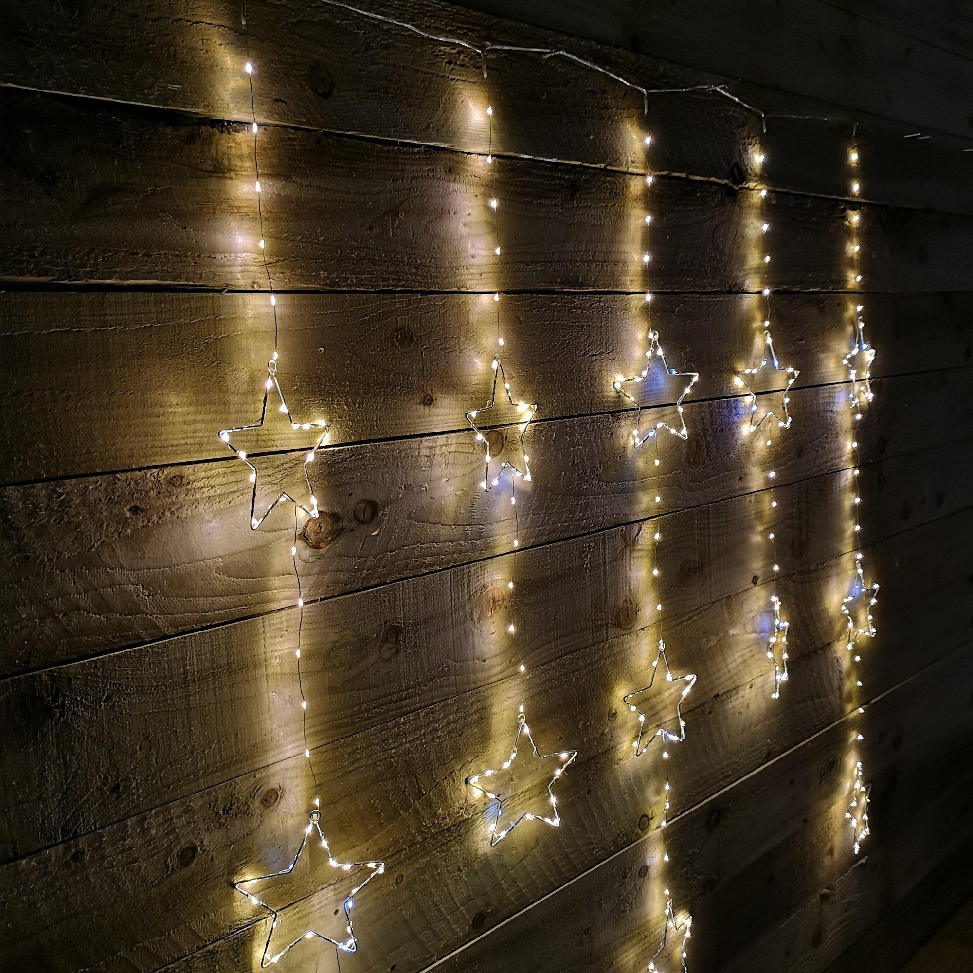 Flashing star LED curtain lights in white mix, featuring multiple star shapes strung along a warm white wire, displayed against a rustic wooden backdrop.