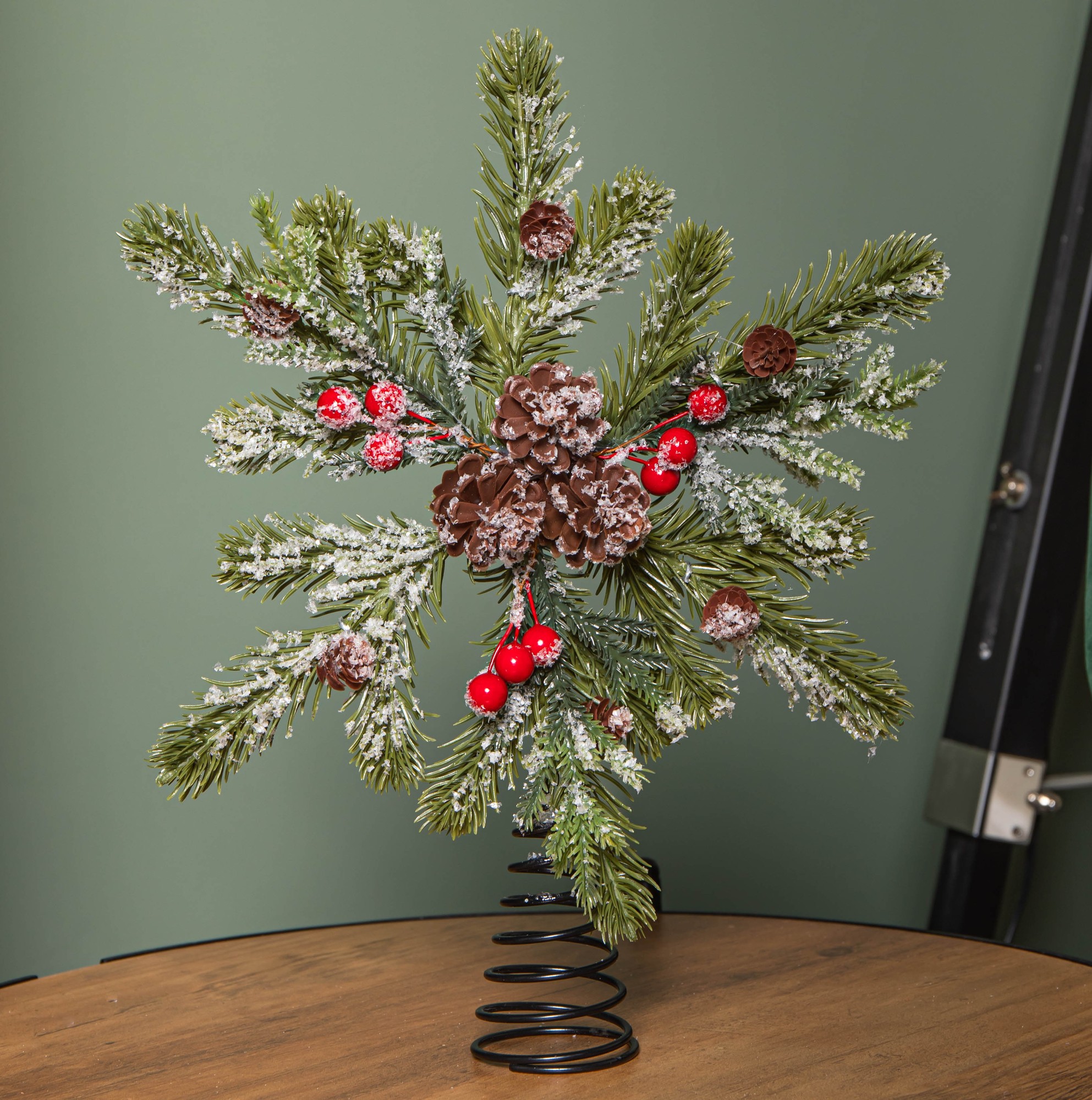 A festive 33cm Christmas tree topper featuring frosted green foliage, pinecones, and red berries, mounted on a black spiral base.