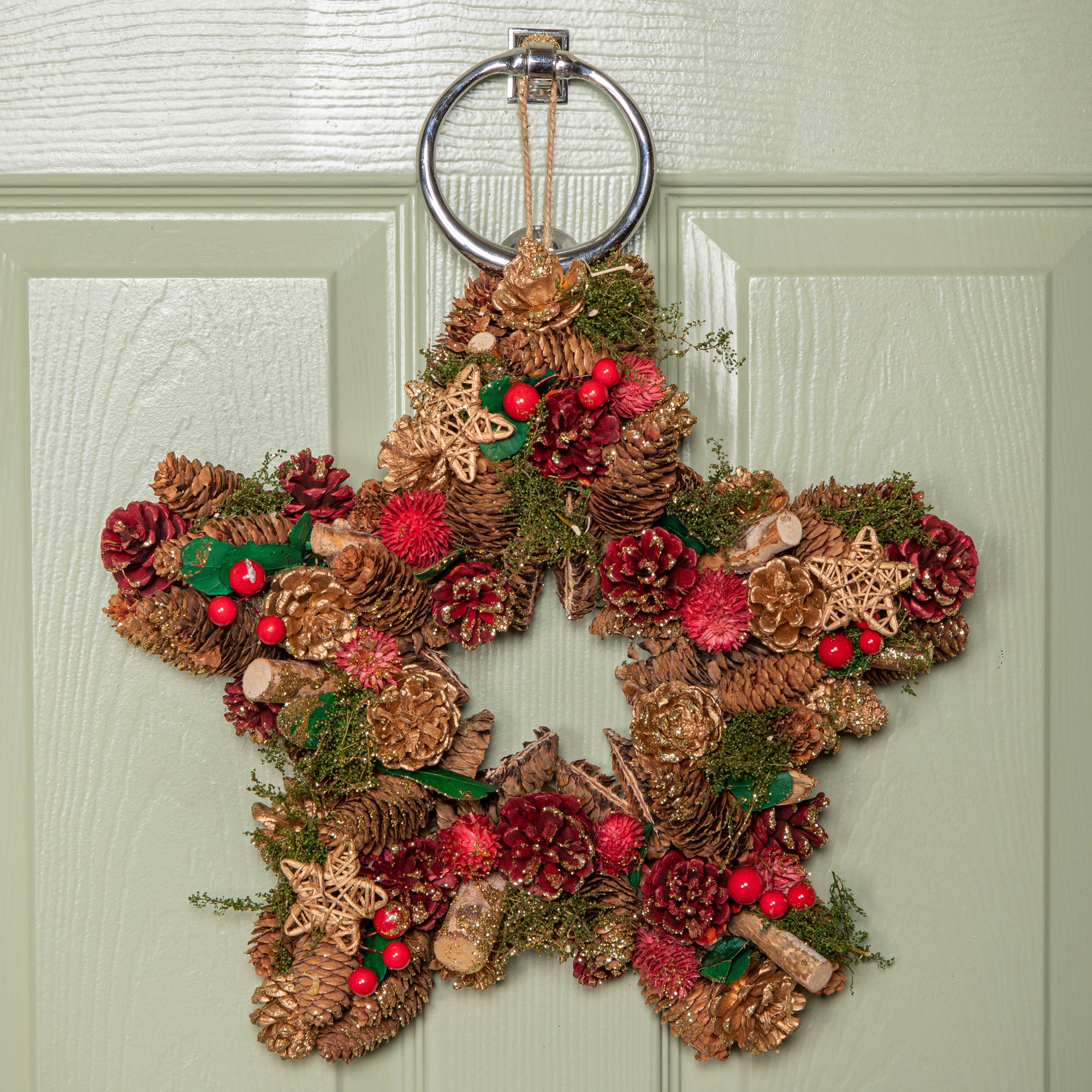 35cm red star-shaped Christmas wreath adorned with red berries, pinecones, and decorative wooden stars, featuring a metal ring for hanging.