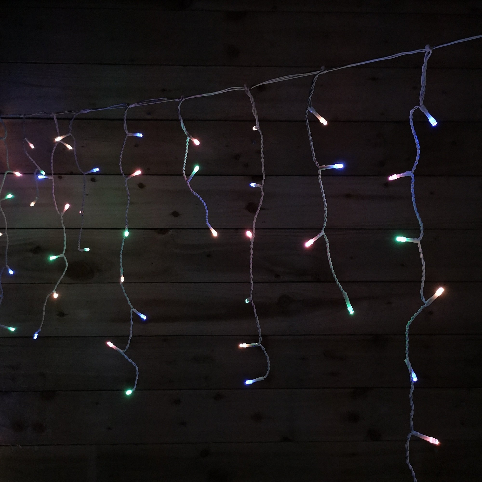 Multifunctional pastel icicle lights with 600 LED bulbs in various colors, hanging from a white cord against a dark wooden background, suitable for indoor and outdoor use.