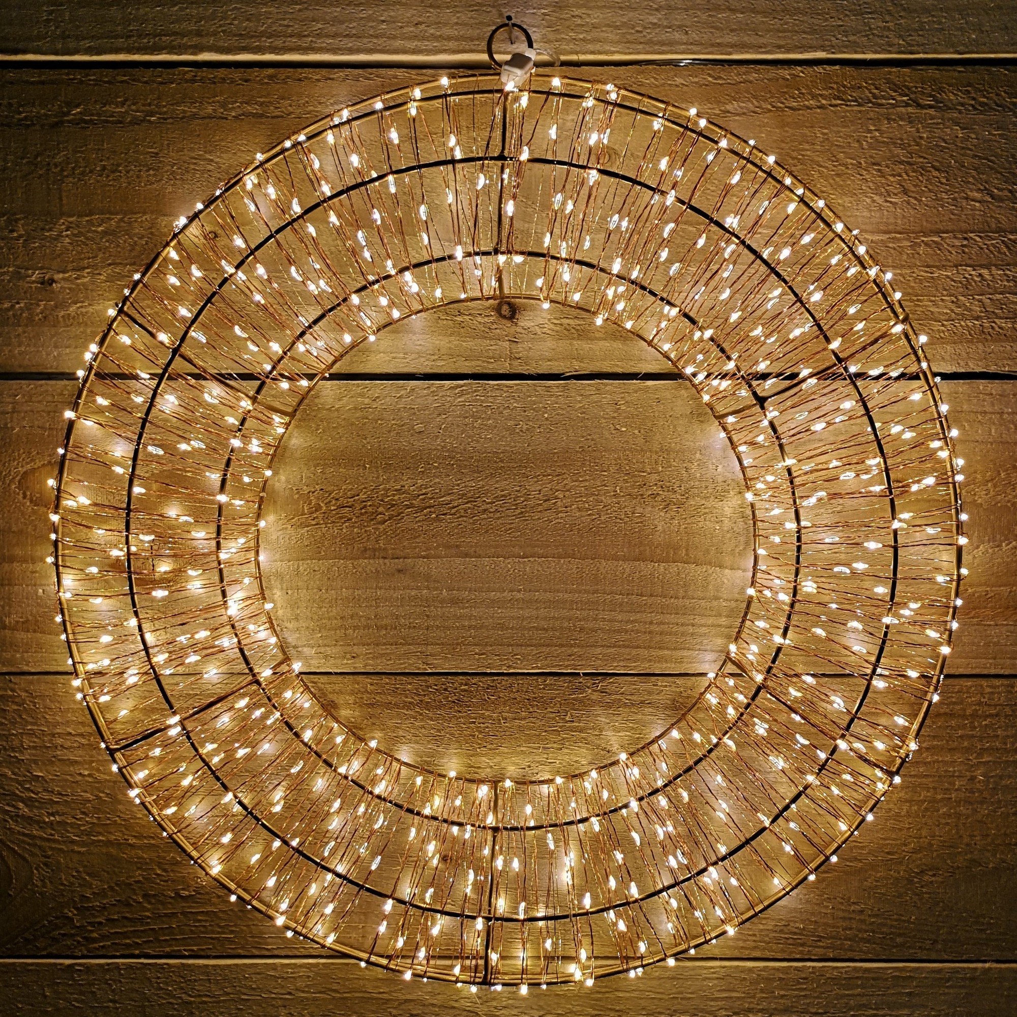 Rose gold metal wreath adorned with 600 warm white LED bulbs, measuring 45cm in diameter, set against a rustic wooden background.