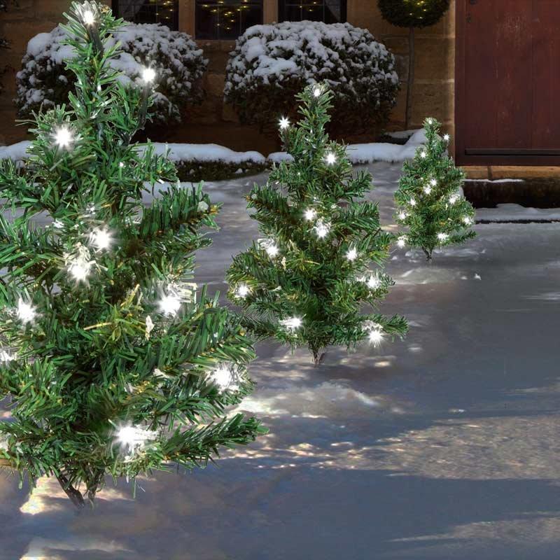 Six small artificial green Christmas trees with white LED lights, arranged along a snowy outdoor path, creating a festive ambiance.