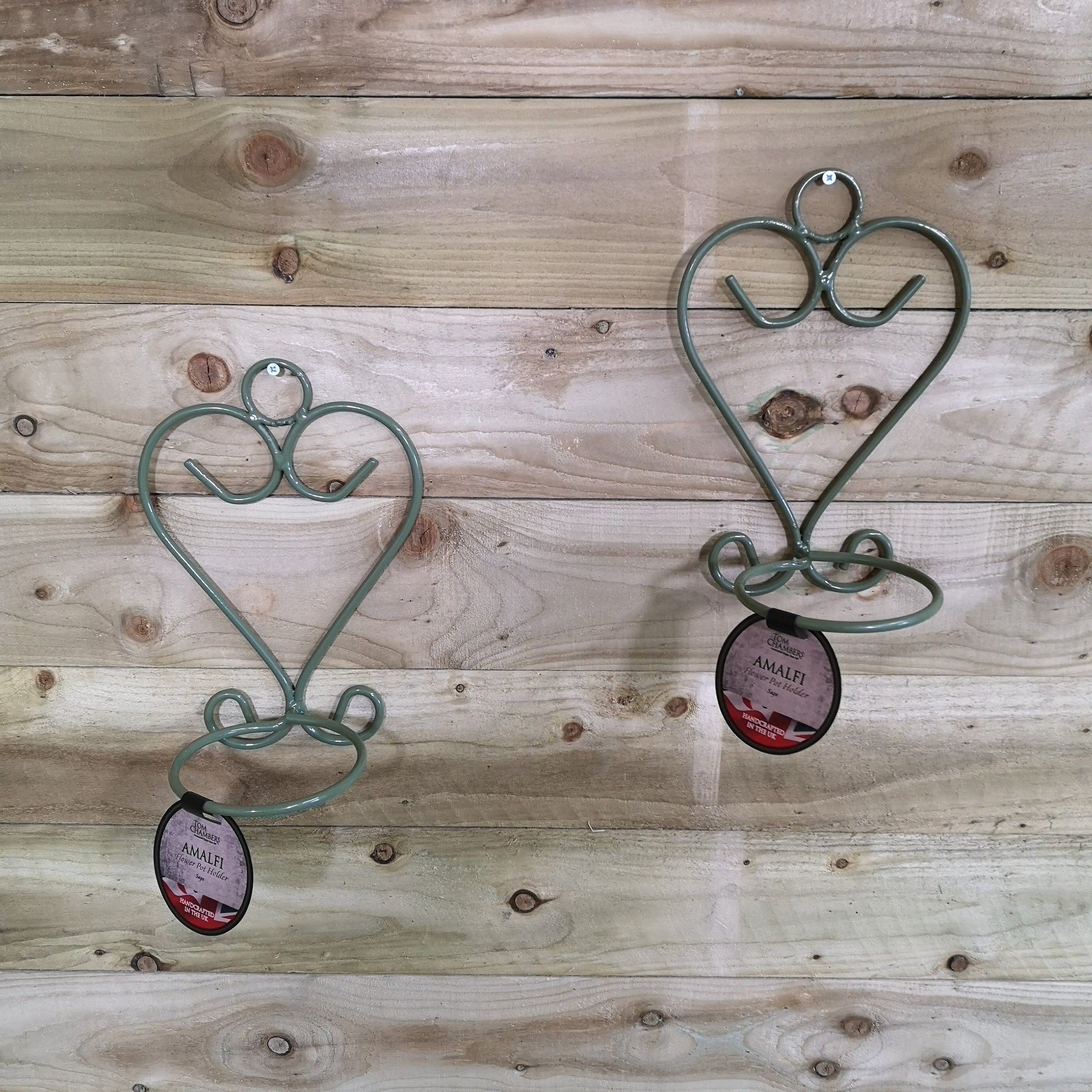Handcrafted sage green metal wall mount holders for herb or flower pots, featuring a heart design and circular base, displayed against a rustic wooden background.