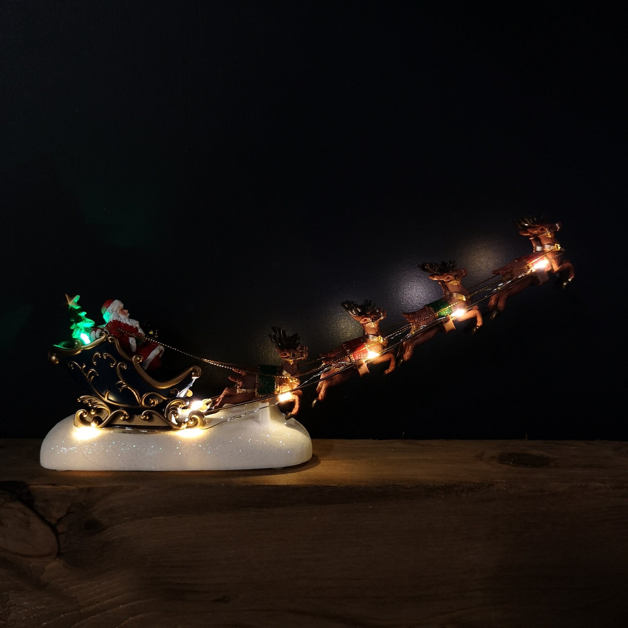 34cm battery-operated Christmas decoration featuring a light-up Santa in a sleigh, pulled by five reindeer, with a gold and white design and glowing LED lights.
