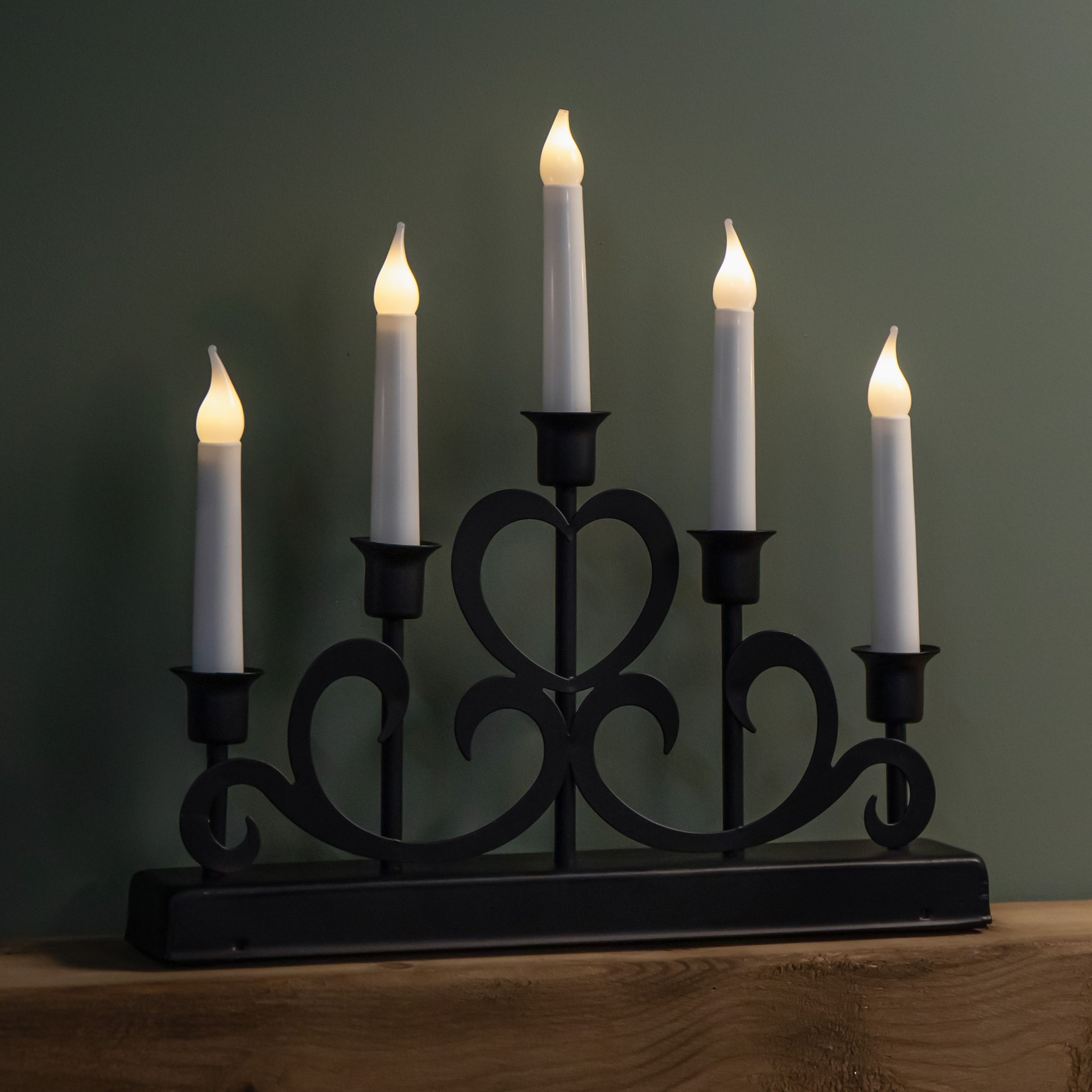Black metal Christmas candlebridge featuring five LED candles with flickering flame tips, elegantly designed with swirling accents, ideal for festive decor.