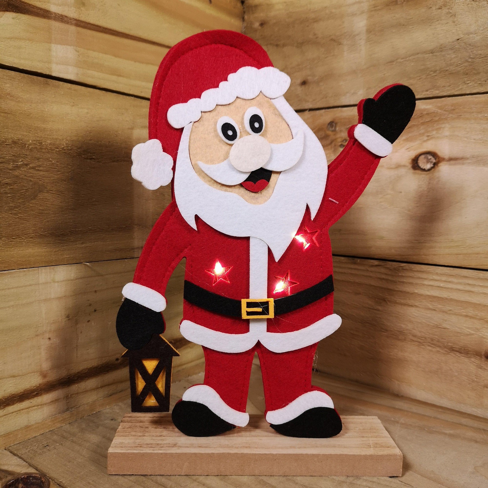 Felt Santa figure in red suit, white beard, and black gloves, waving with a lantern, featuring three warm white LED lights on a wooden base.