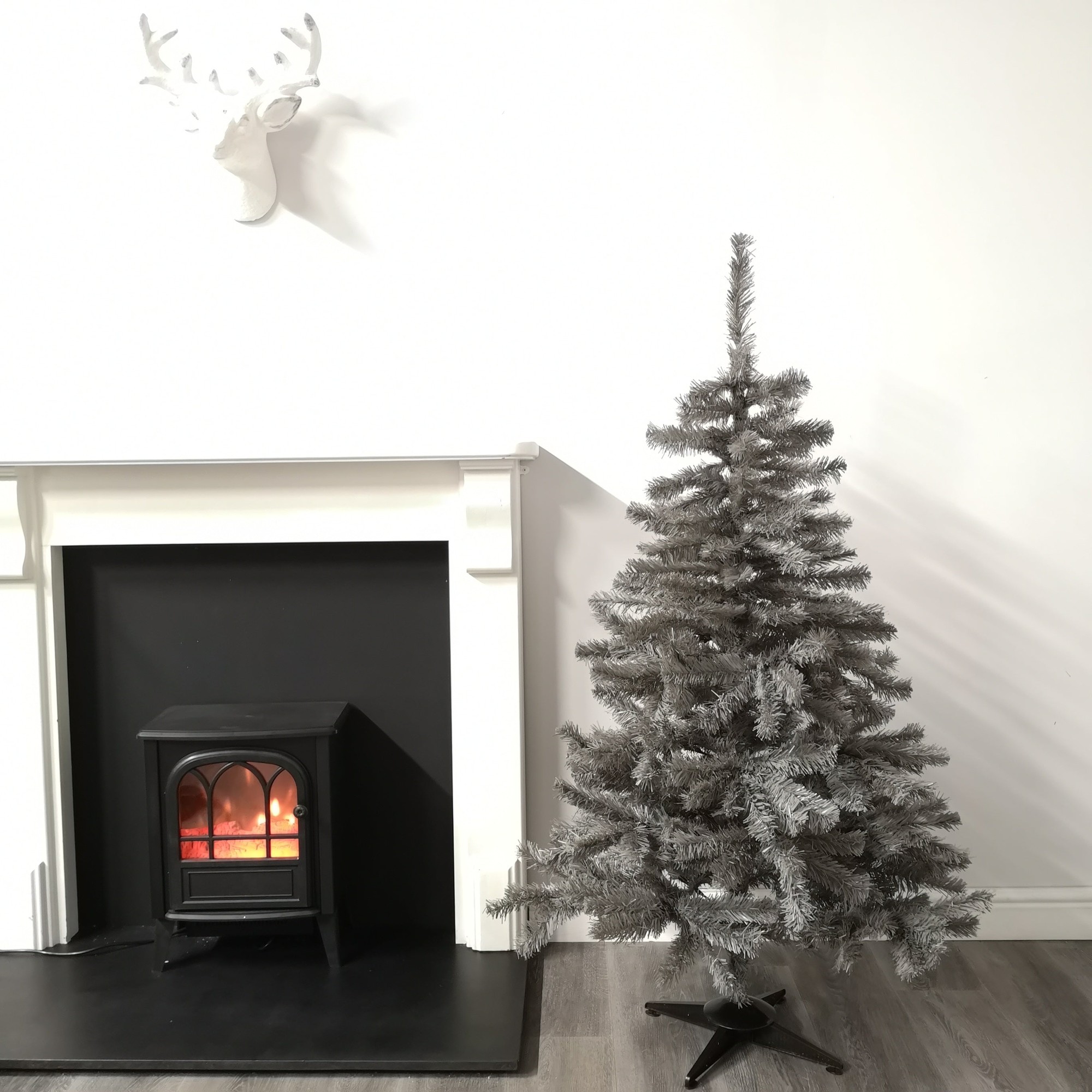 5ft Colorado Grey Spruce Christmas tree with wrapped branches and 339 tips, featuring a soft grey color, standing next to a black fireplace with a glowing flame.