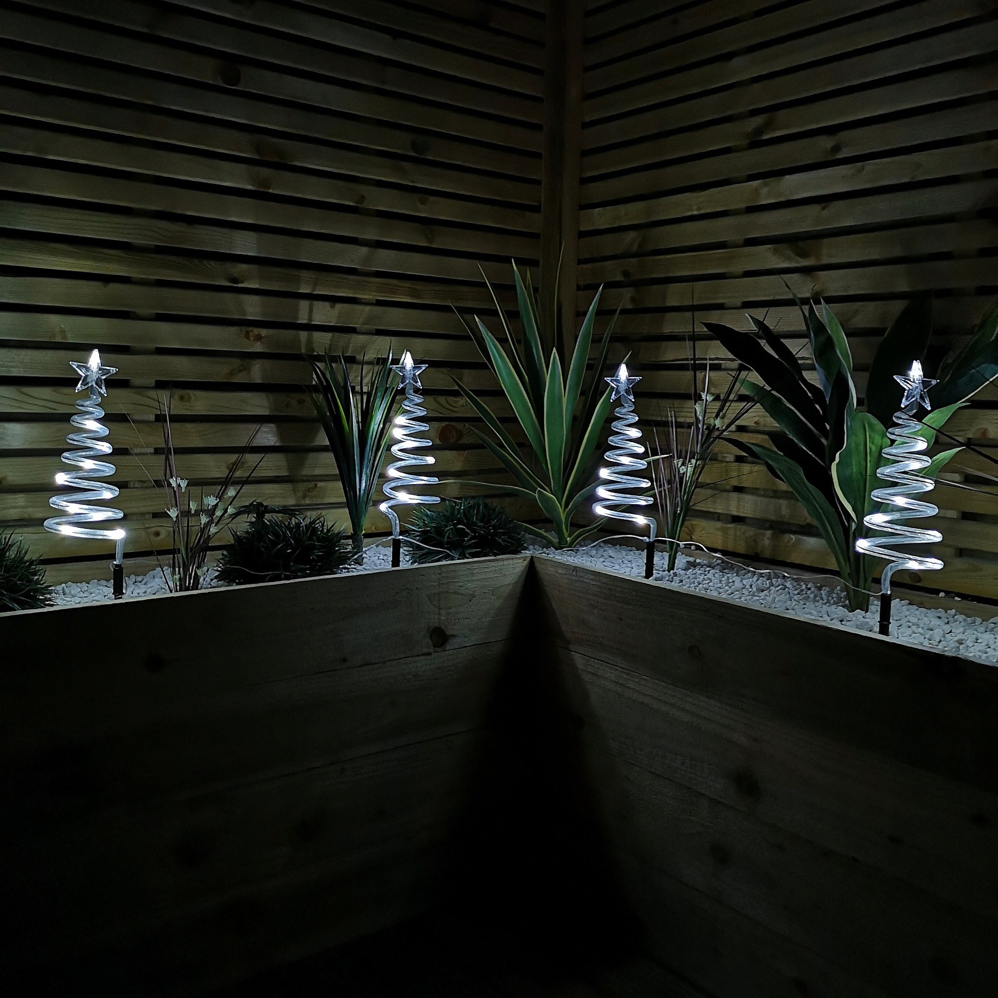 Set of 4 battery-operated LED cool white spiral tree path lights with star tops, featuring a timer, displayed in a planter with green plants and gravel.