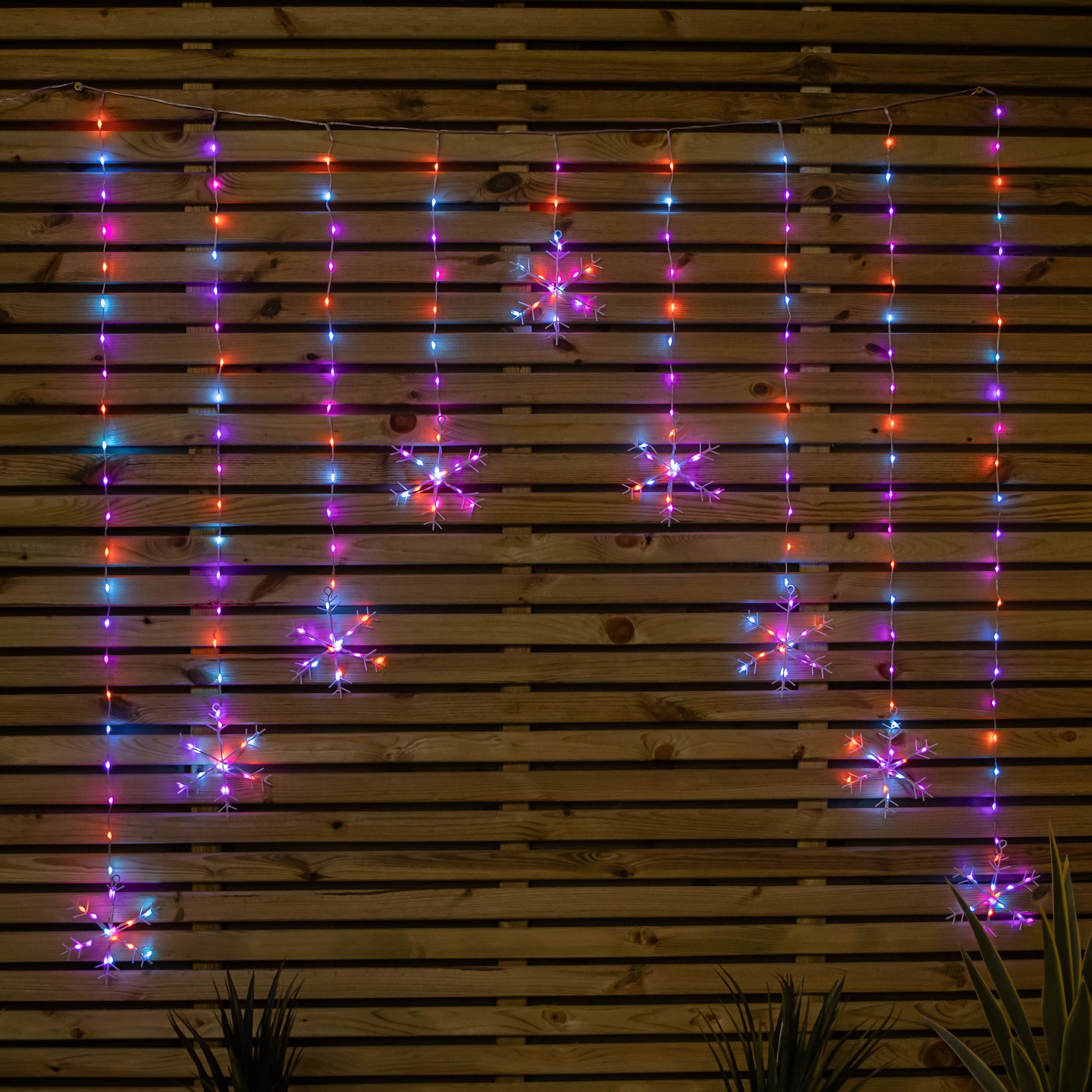 Colorful curtain lights featuring 267 rainbow LEDs in snowflake shapes, hanging from a wooden backdrop, creating a festive atmosphere.
