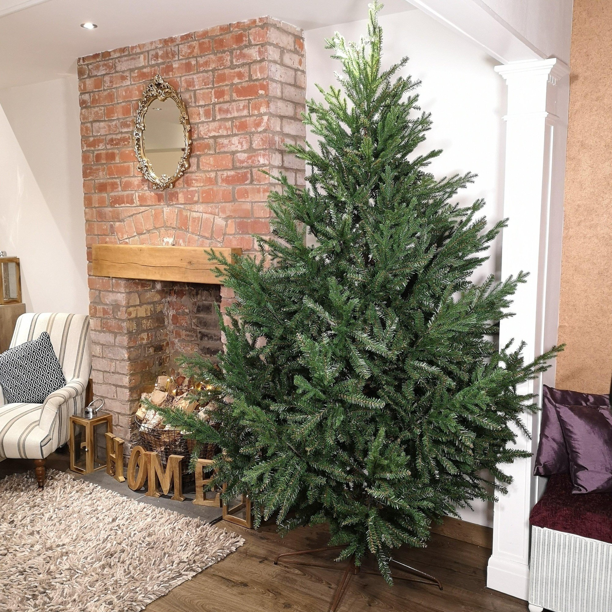 Tall, 8ft green artificial Christmas tree made of PE and PVC, featuring a natural look with dense foliage, positioned beside a brick fireplace and decorative elements.