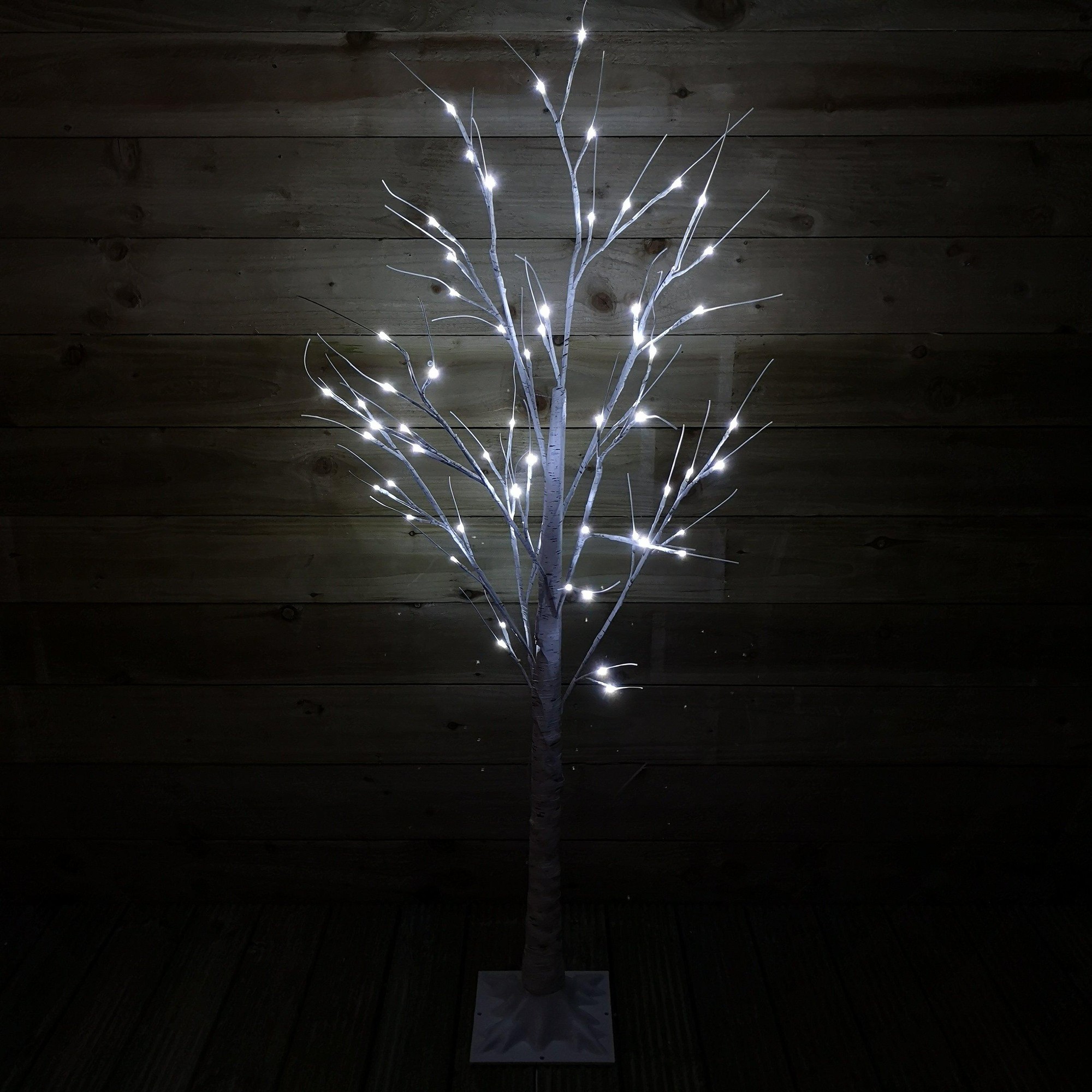 A 1.5m tall birch tree with white branches, featuring 64 ice white LED lights, set against a dark wooden background, ideal for indoor or outdoor Christmas decor.