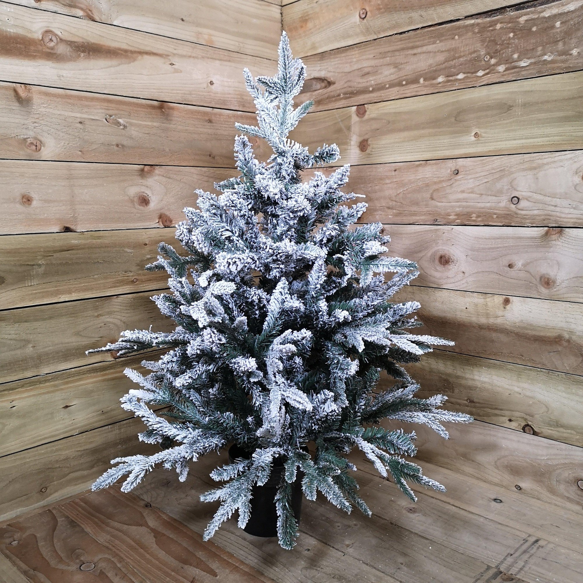 Snowy green 90cm flocked mini Christmas tree in a black pot, featuring frosted branches and a full, bushy appearance, set against a rustic wooden background.