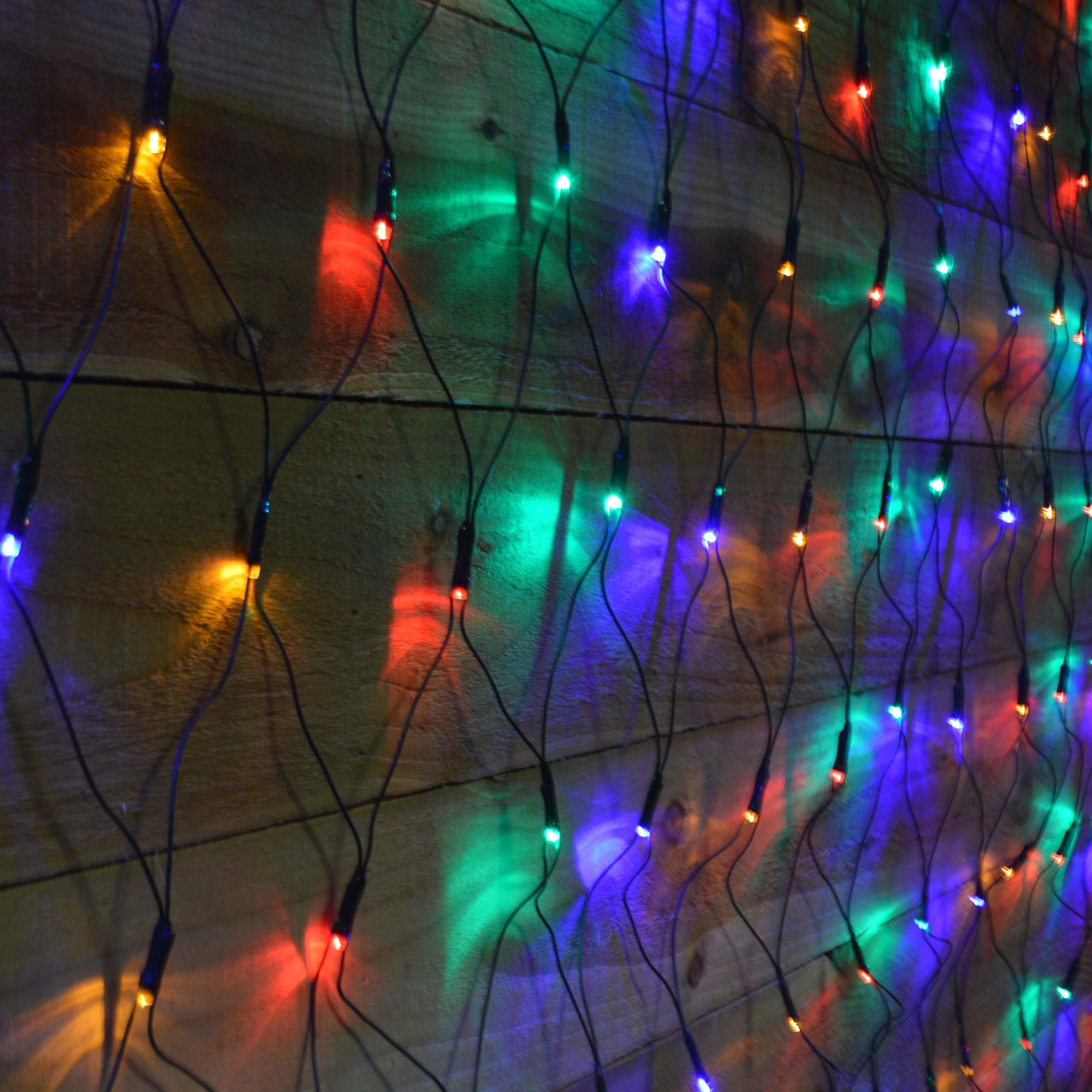 Multicolored 360 LED Christmas net lights measuring 3.5m x 1.2m, featuring bright red, green, blue, and yellow bulbs on a dark wire, arranged in a net pattern against a wooden background.