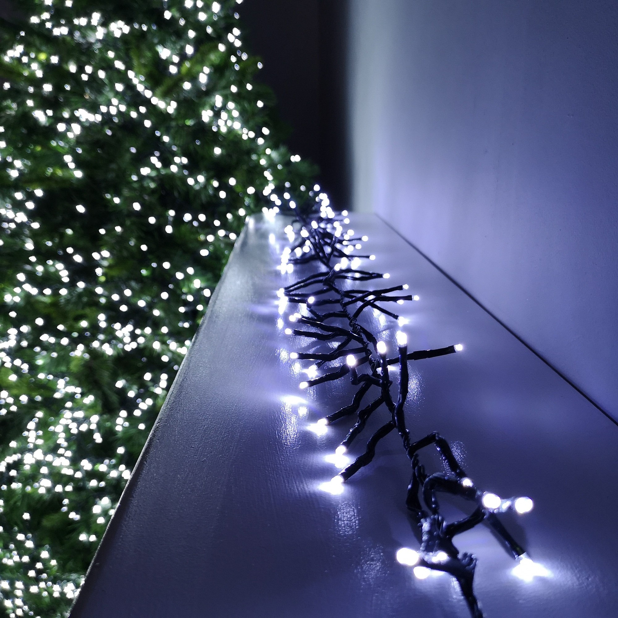 62.5m string lights with 5000 white LED bulbs on a black wire, featuring multi-action settings and a timer, displayed against a blurred backdrop of a lit Christmas tree.