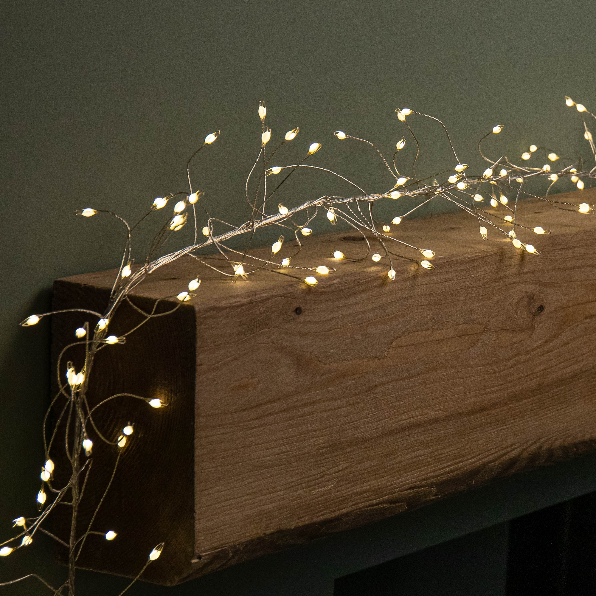 5.4m garland with 860 warm white LED lights on flexible silver wire, featuring delicate, glowing bulb shapes, elegantly draped over a wooden surface.