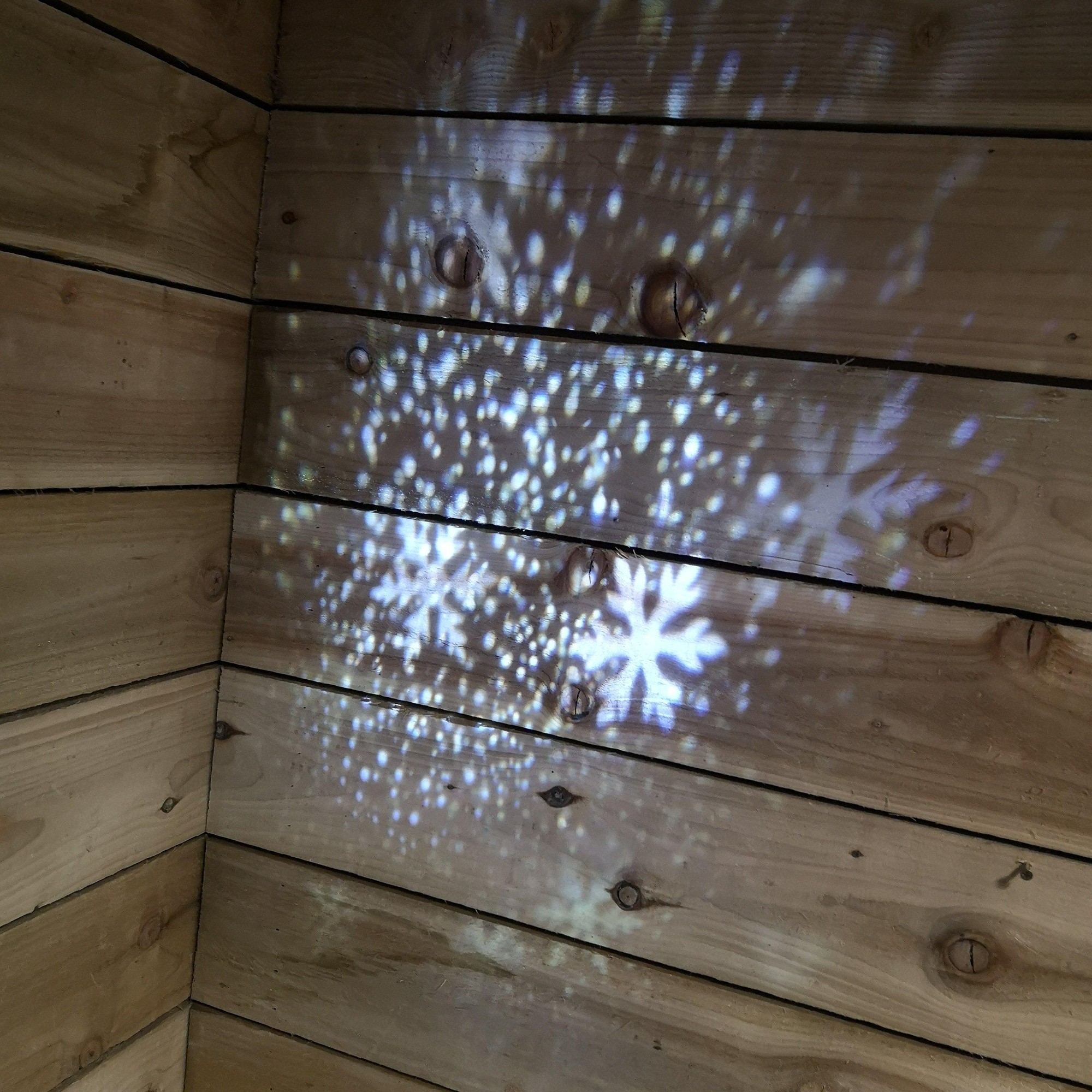 Snowflake patterns projected in white and blue light onto wooden walls, showcasing the Premier LED 31cm Snowstorm Projector by Samuel Alexander.