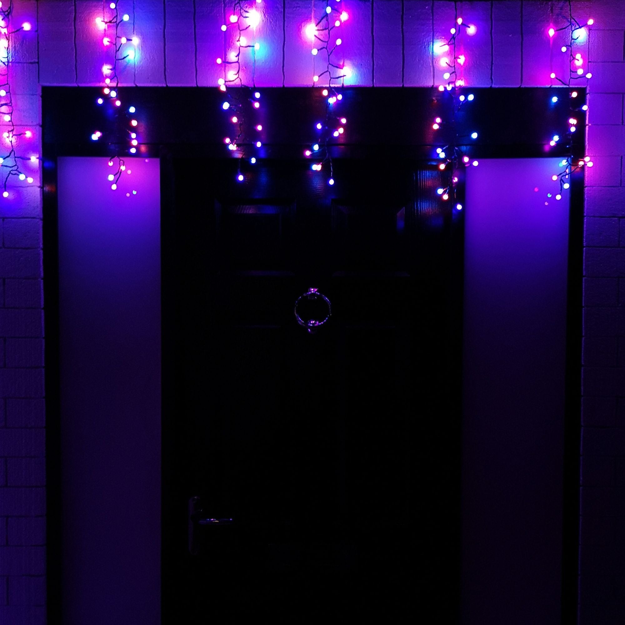 Multi-function LED cluster curtain lights in rainbow colors, featuring vibrant purple, blue, and pink hues, draped above a black door, ideal for Christmas decorations.