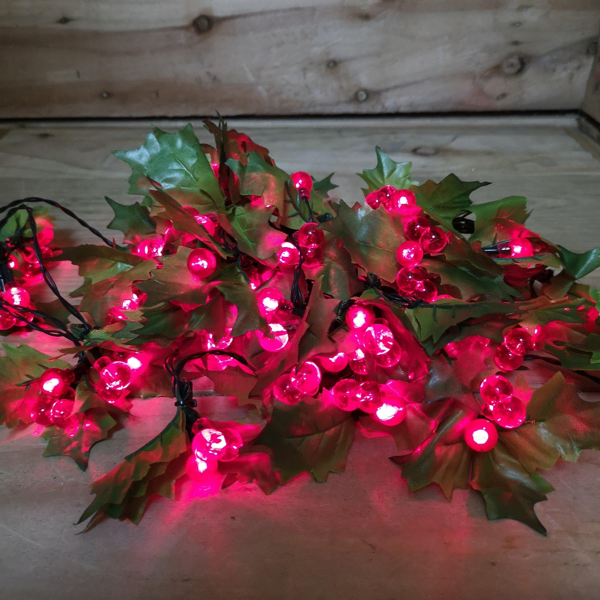 100 red berry and holly LED lights on a green cable, featuring vibrant red bulbs surrounded by green holly leaves, ideal for festive decorations.