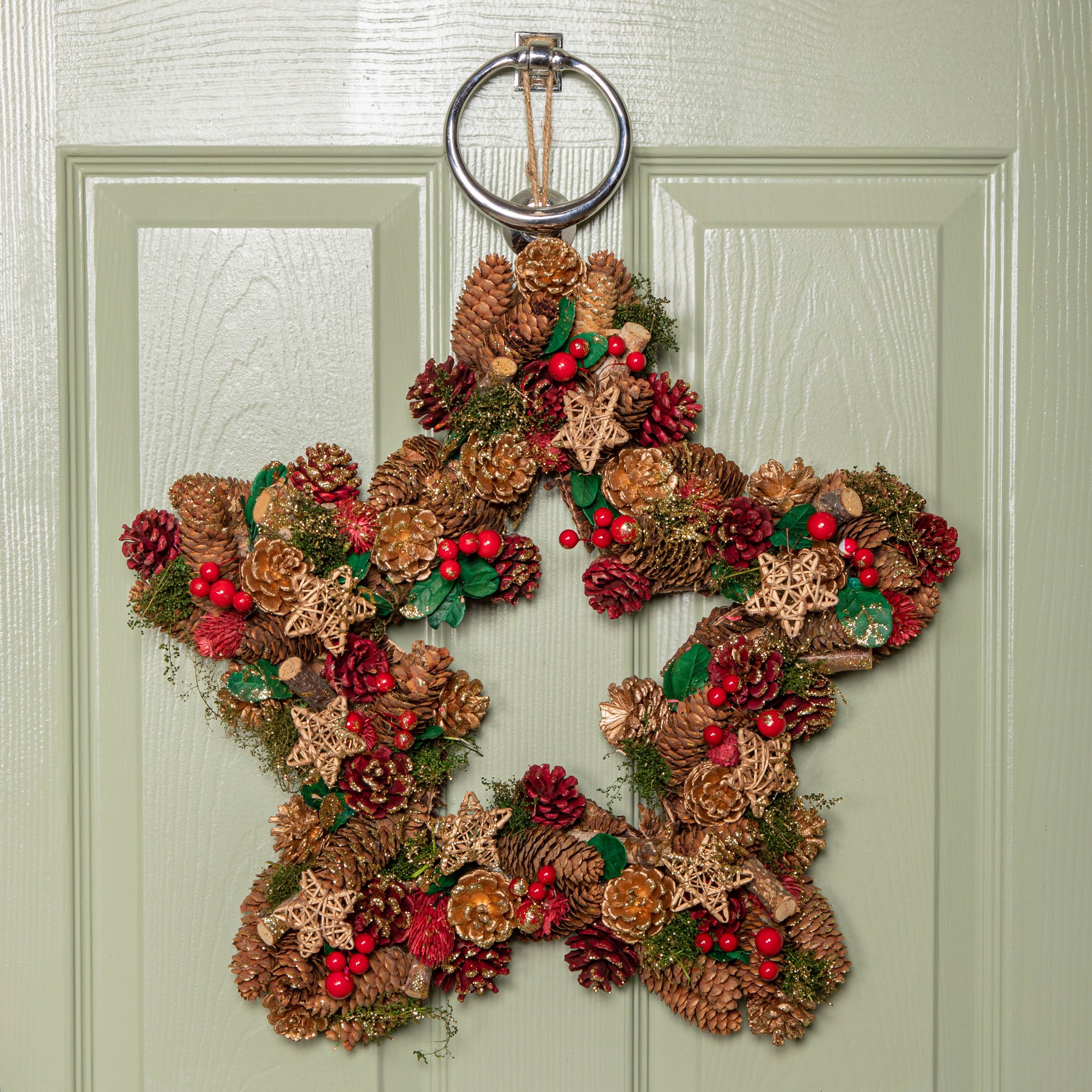A 45cm red hanging star wreath adorned with red berries, pinecones, and golden stars, featuring a metal ring for hanging against a light green door.