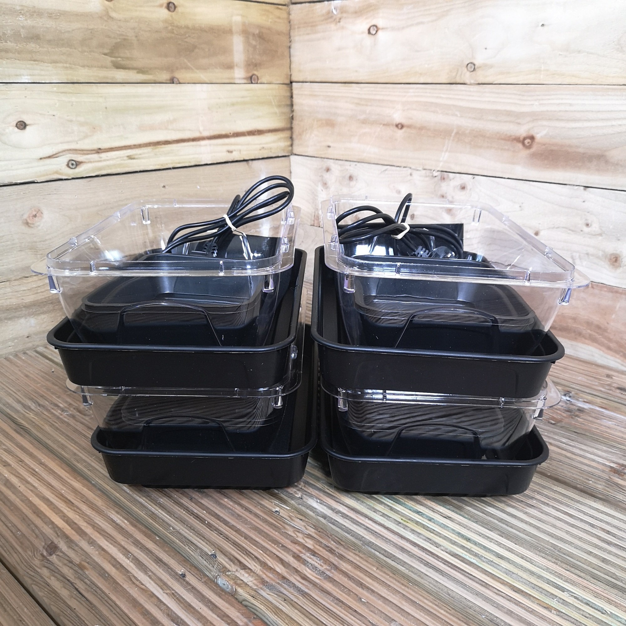 Four black heated seed starter trays with transparent lids, featuring two trays stacked on top of each other, designed for indoor seedling planting.
