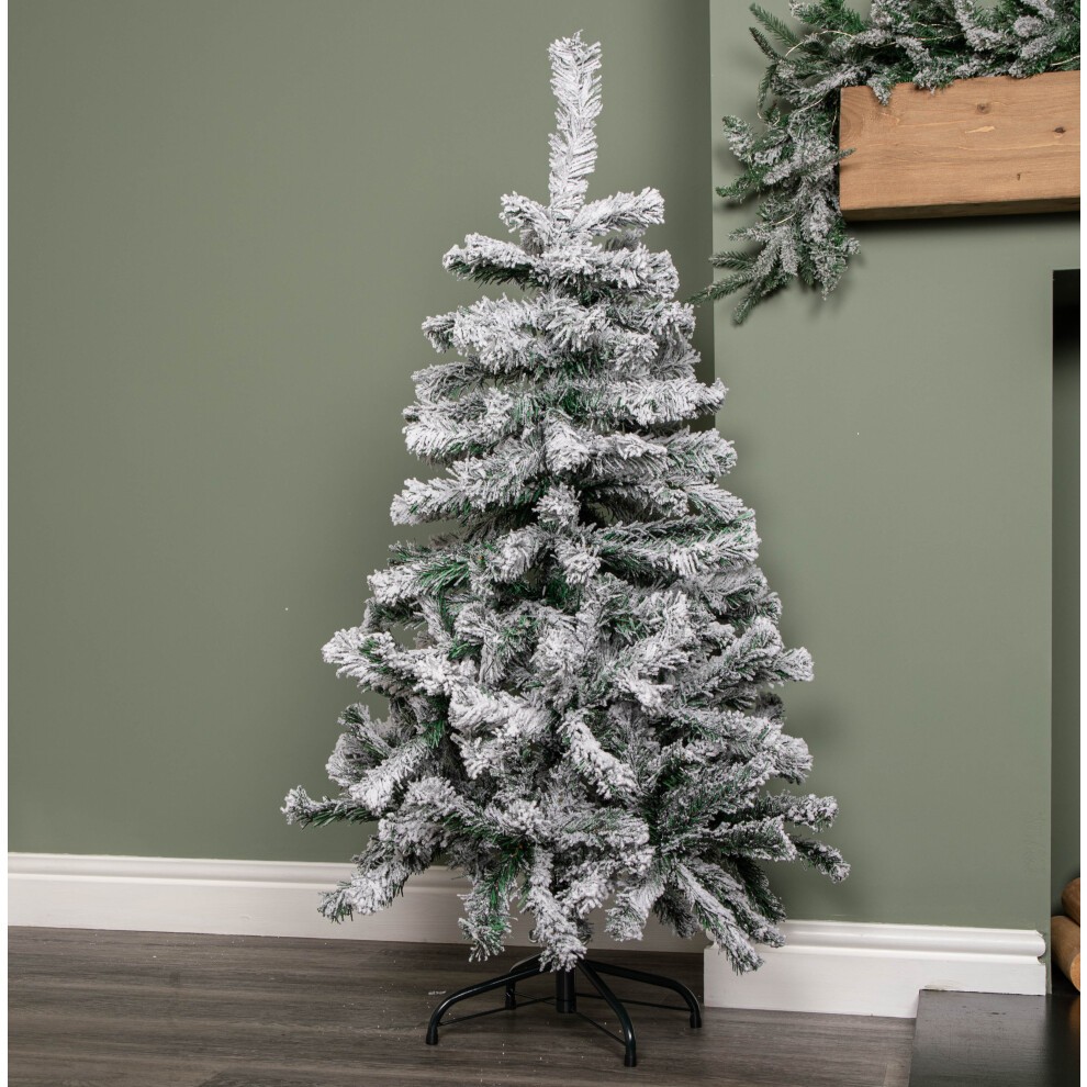 Snow flocked artificial Christmas tree standing 4 feet tall, featuring 177 tips, a green metal stand, and a frosted white appearance, set against a green wall.
