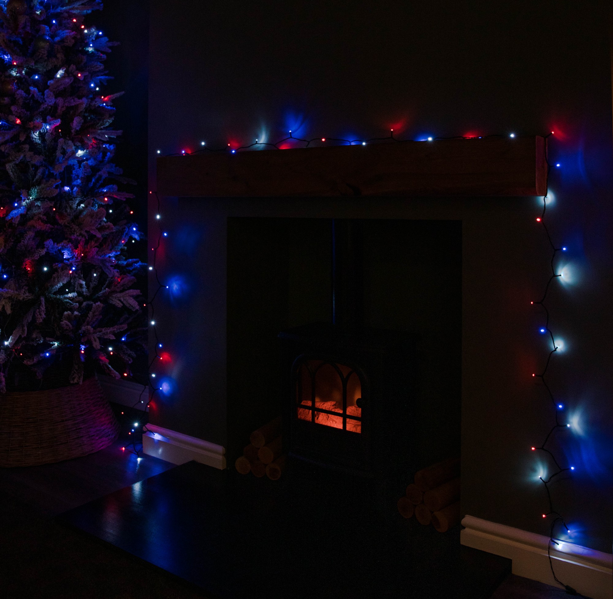 Multi-action Christmas string lights featuring 480 LED bulbs in blue, red, and white, draped around a fireplace and a decorated tree, creating a festive ambiance.