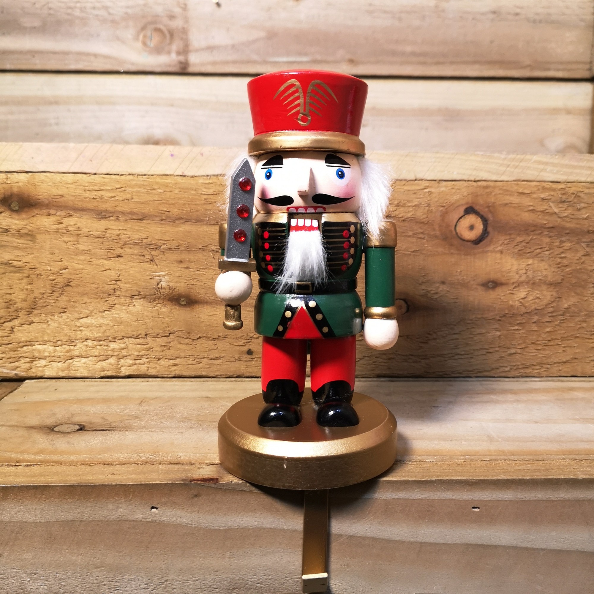 24cm wooden nutcracker stocking holder featuring a soldier in red and green attire, holding a sword, with a gold base and detailed facial features.