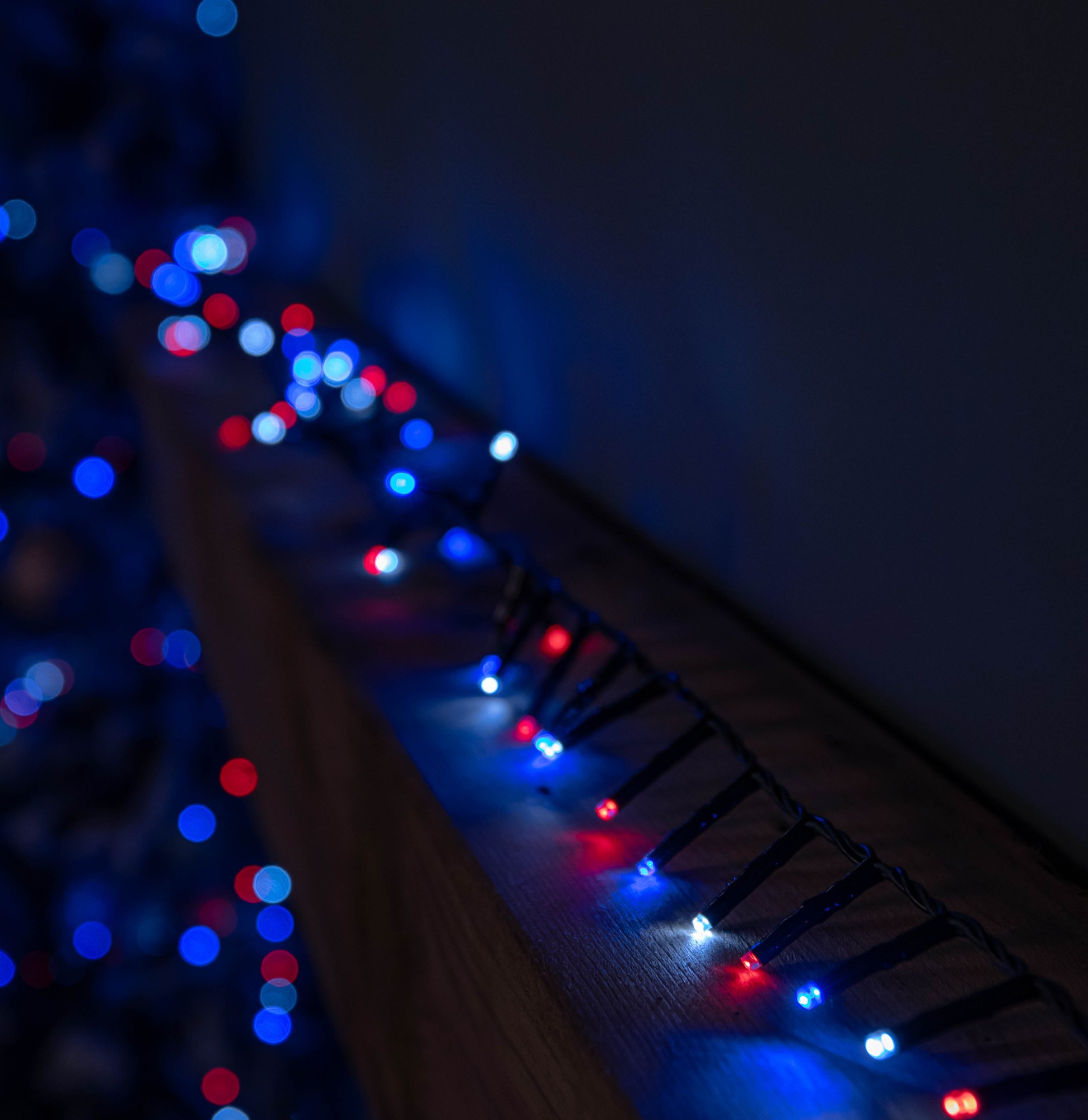 12.5m string lights featuring 500 LED bulbs in blue, white, and red, with a timer function, set against a dark background and draped along a wooden surface.