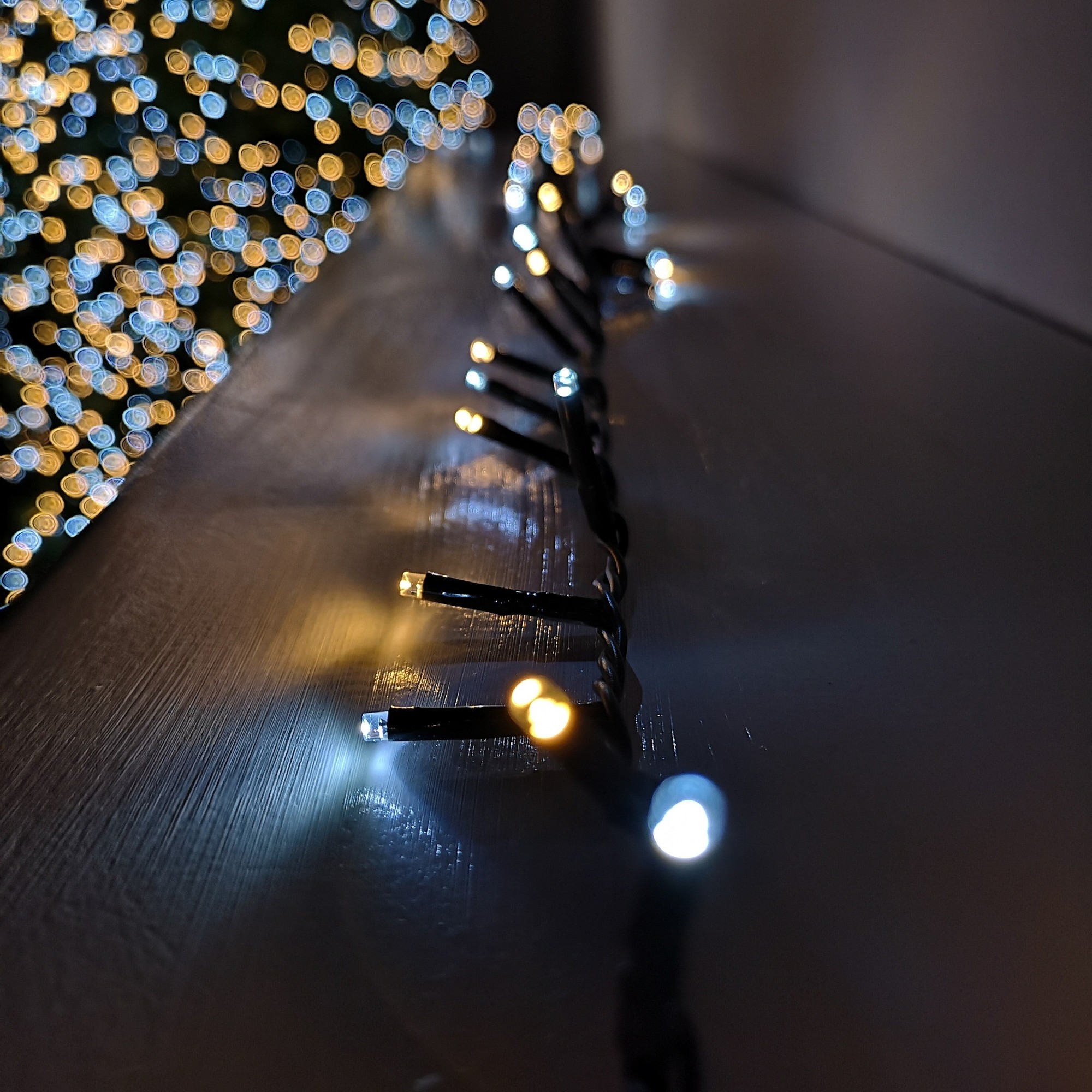 Multi-action Christmas string lights featuring 240 LED bulbs in white and warm white, with a dark wire, showcasing a soft glow against a blurred festive background.