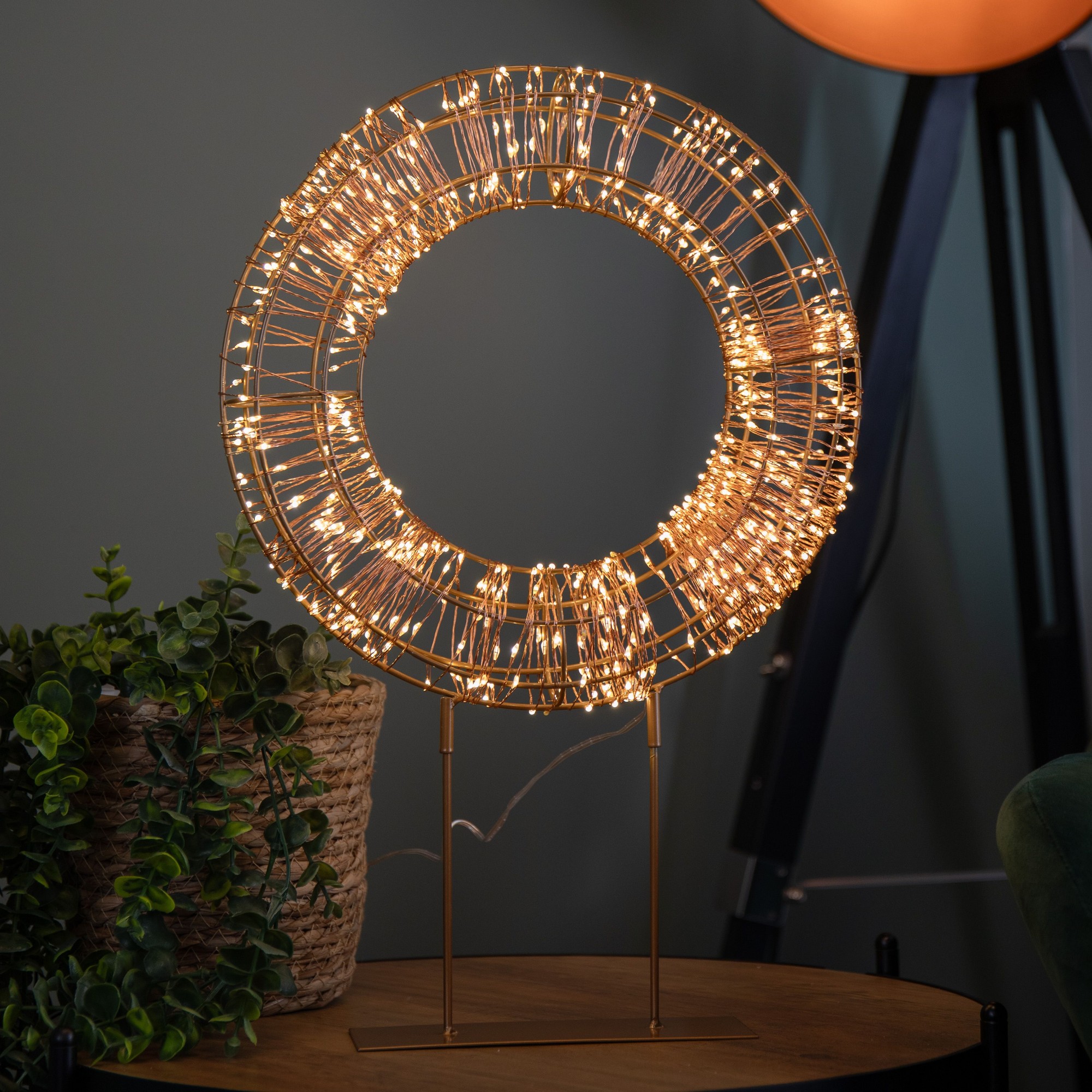 45cm rose gold Christmas wreath on a metal stand, featuring twinkling warm white LEDs, set against a dark green background with greenery nearby.