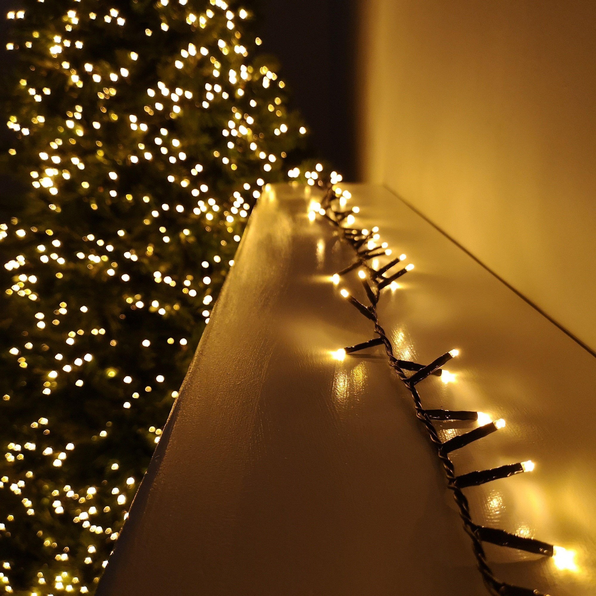 Vintage gold string lights with 1000 LED bulbs, 25 meters long, featuring a timer function, elegantly draped along a surface with a softly lit Christmas tree in the background.