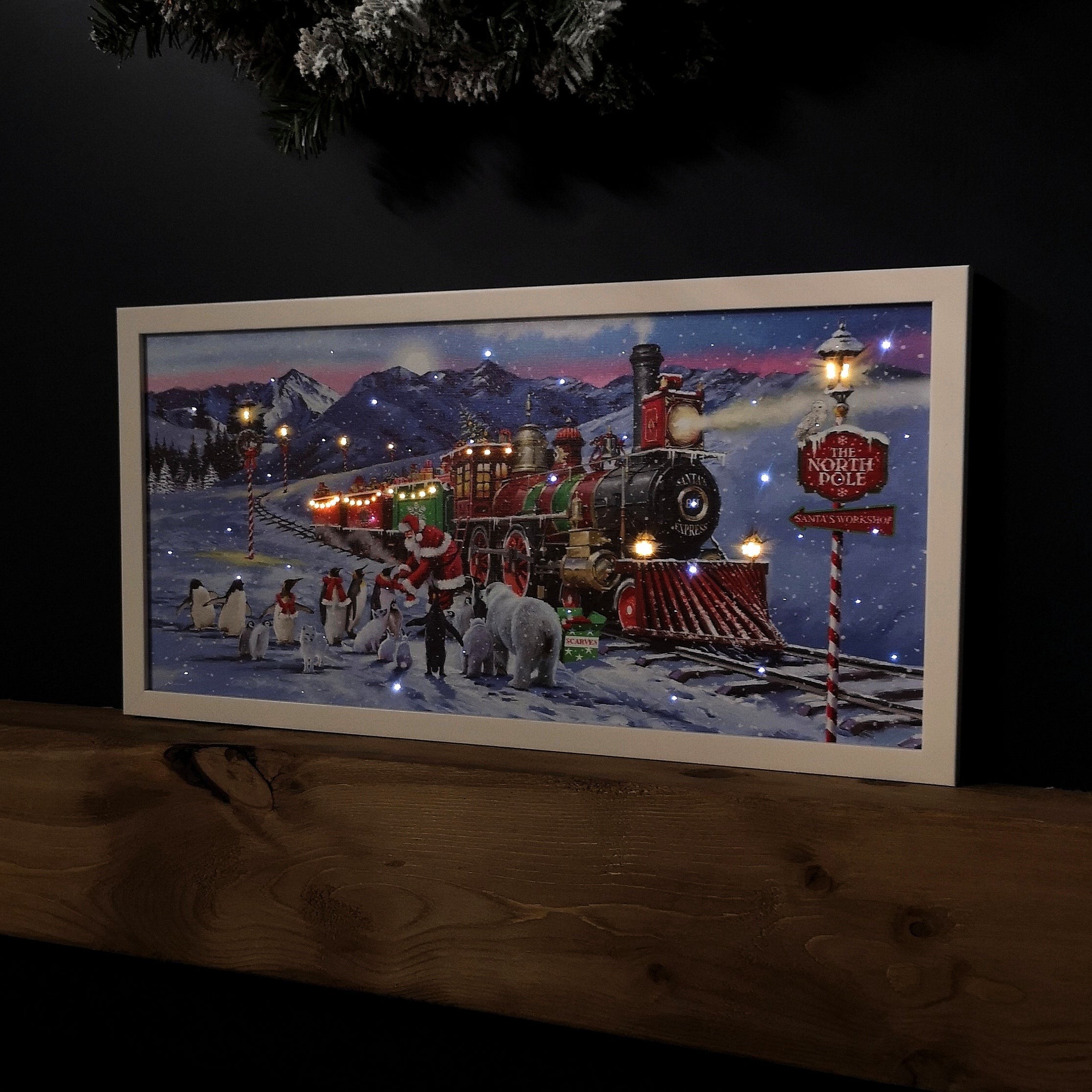 Battery-operated canvas featuring a colorful North Pole Express train with Santa, surrounded by snow, penguins, and mountains, illuminated by warm lights.