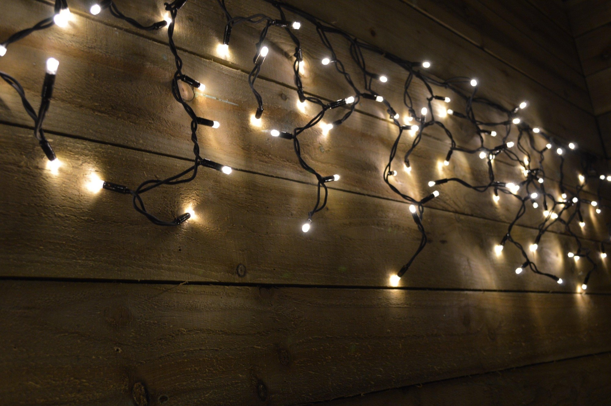 Warm white LED icicle lights on a black cable, featuring 300 bulbs strung along a dark wooden surface, creating a cozy, festive ambiance.