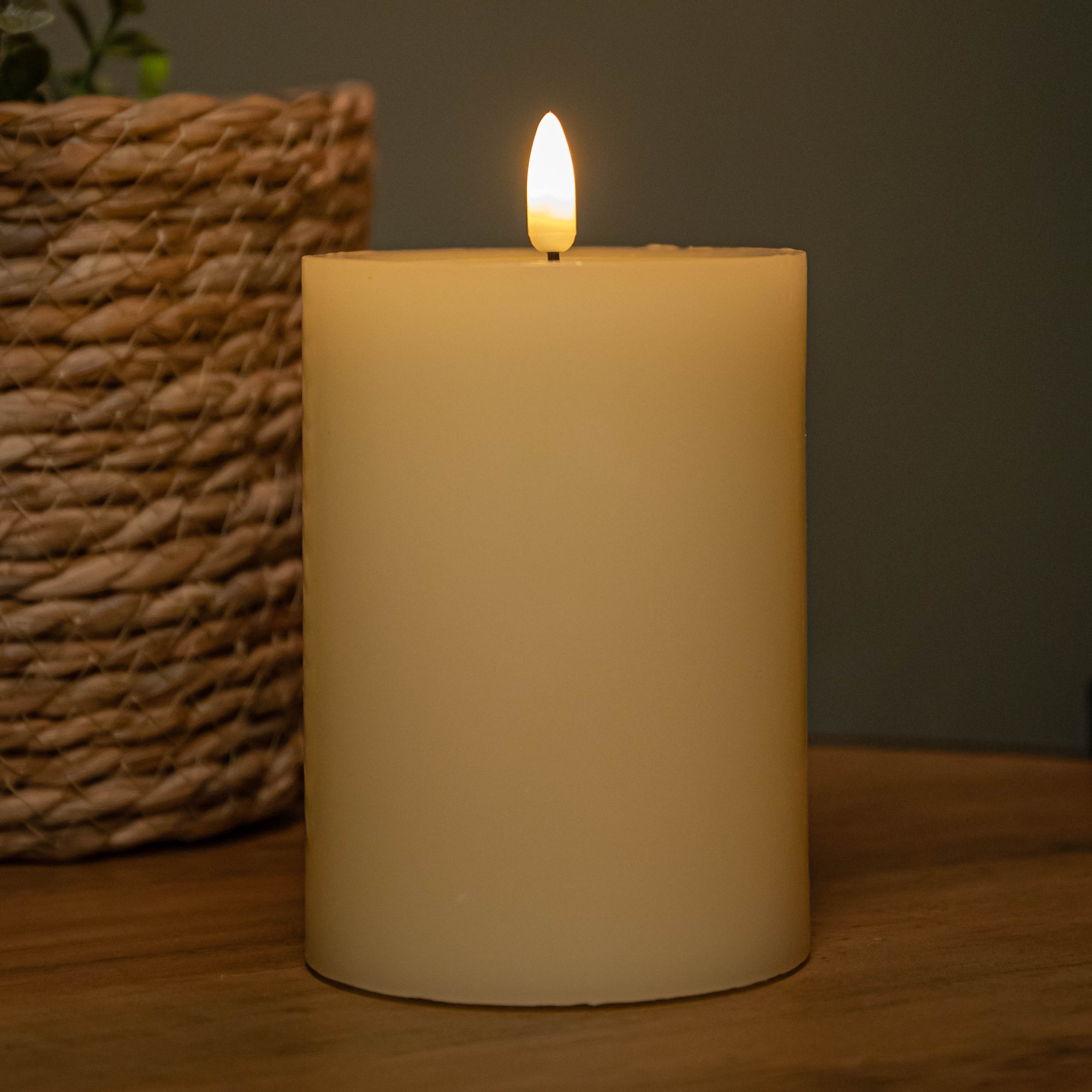 Cream wax candle with a melted pool effect, 9cm x 13cm, featuring a warm white LED flame, set on a wooden surface beside a woven basket.