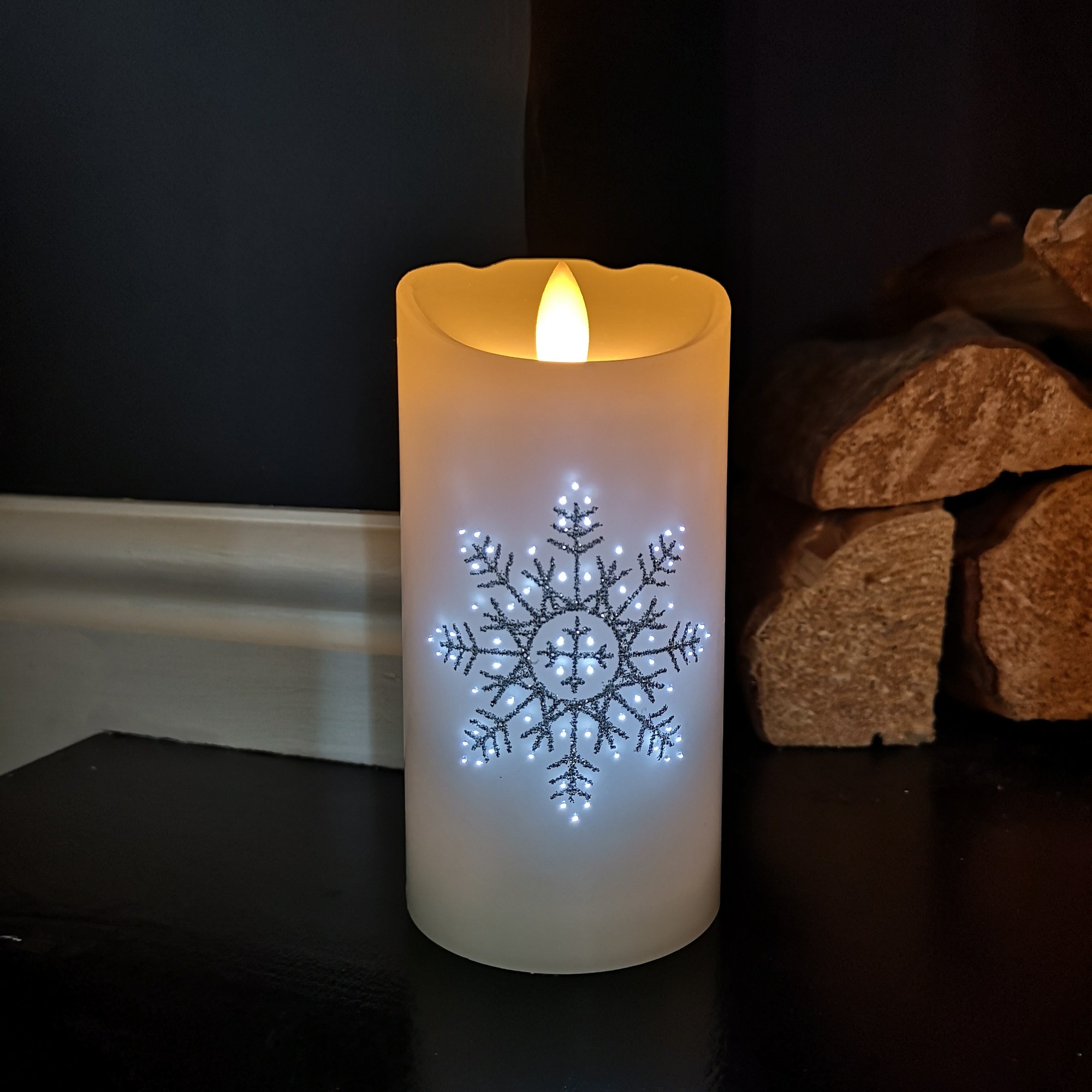 Battery-operated 15cm LED candle featuring a glittery snowflake design, with a warm glowing flame effect and a smooth white wax finish, set against a dark background.