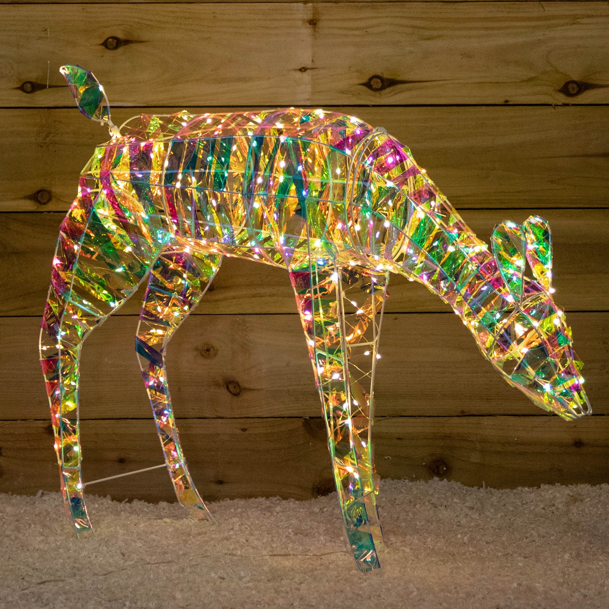 A 65cm iridescent shimmer Christmas reindeer made of translucent material, illuminated by 300 warm white LEDs, displaying vibrant colors against a wooden backdrop.