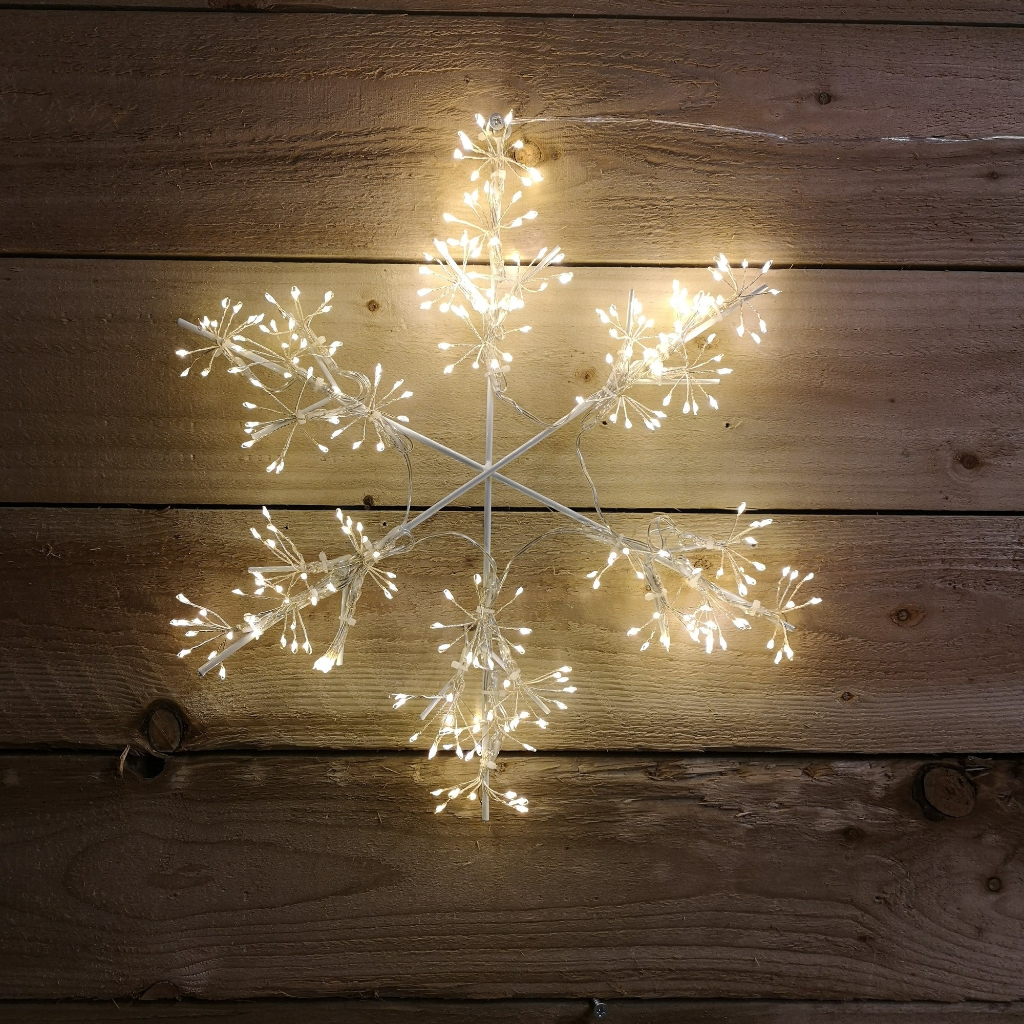 Warm white LED snowflake silhouette with 300 microbrights, featuring delicate branches and a star-like design, mounted against a rustic wooden background.